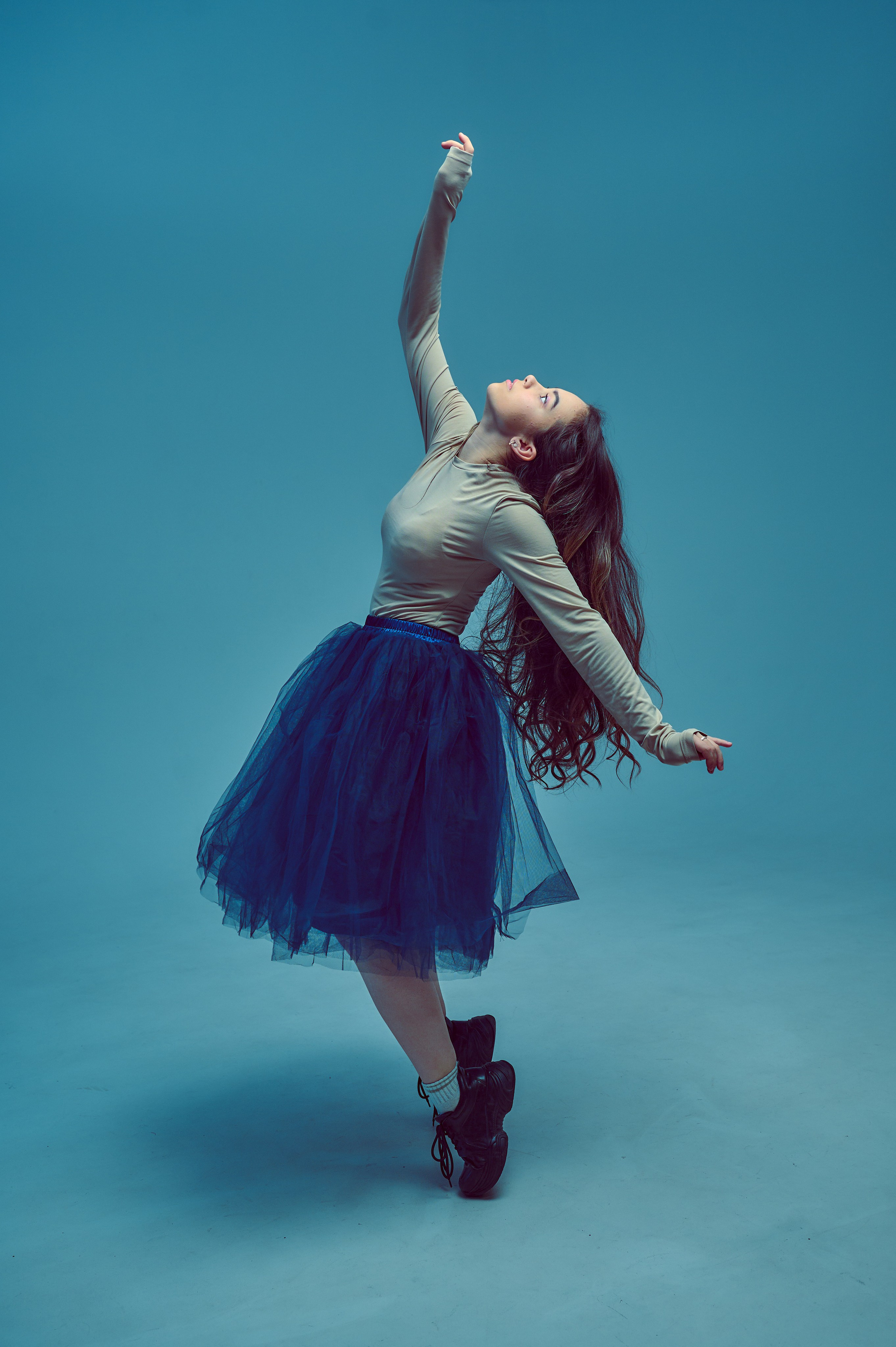 юная девушка в синей юбке тянется рукой вверх, фотосессия в студии на циклораме, голубой фон с помощ9ью света
