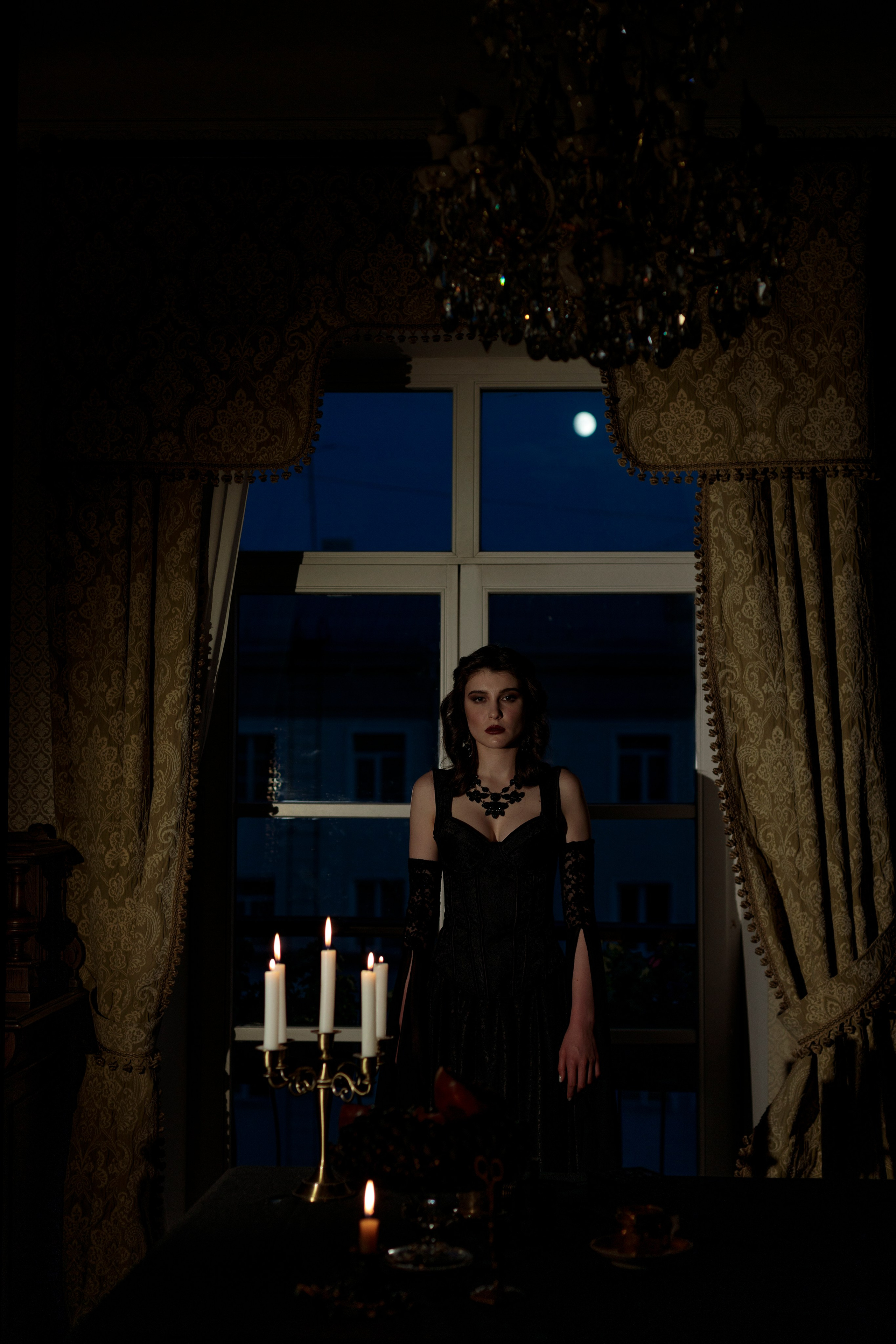 Девушка стоит спиной к окну, за окном светит луна, за окном наступил синий час. Перед девушкой стоит канделябр с горящими свечами.