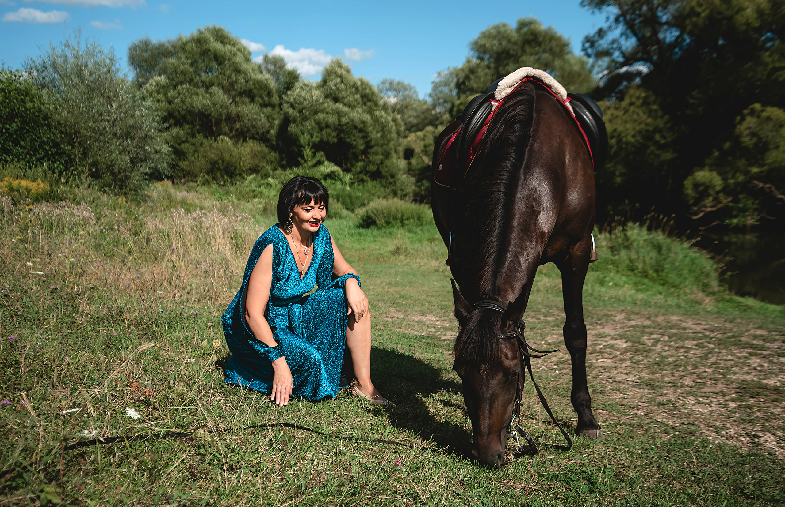 На фото женщина в зеленом платье сидит на коленях  с лошадью.