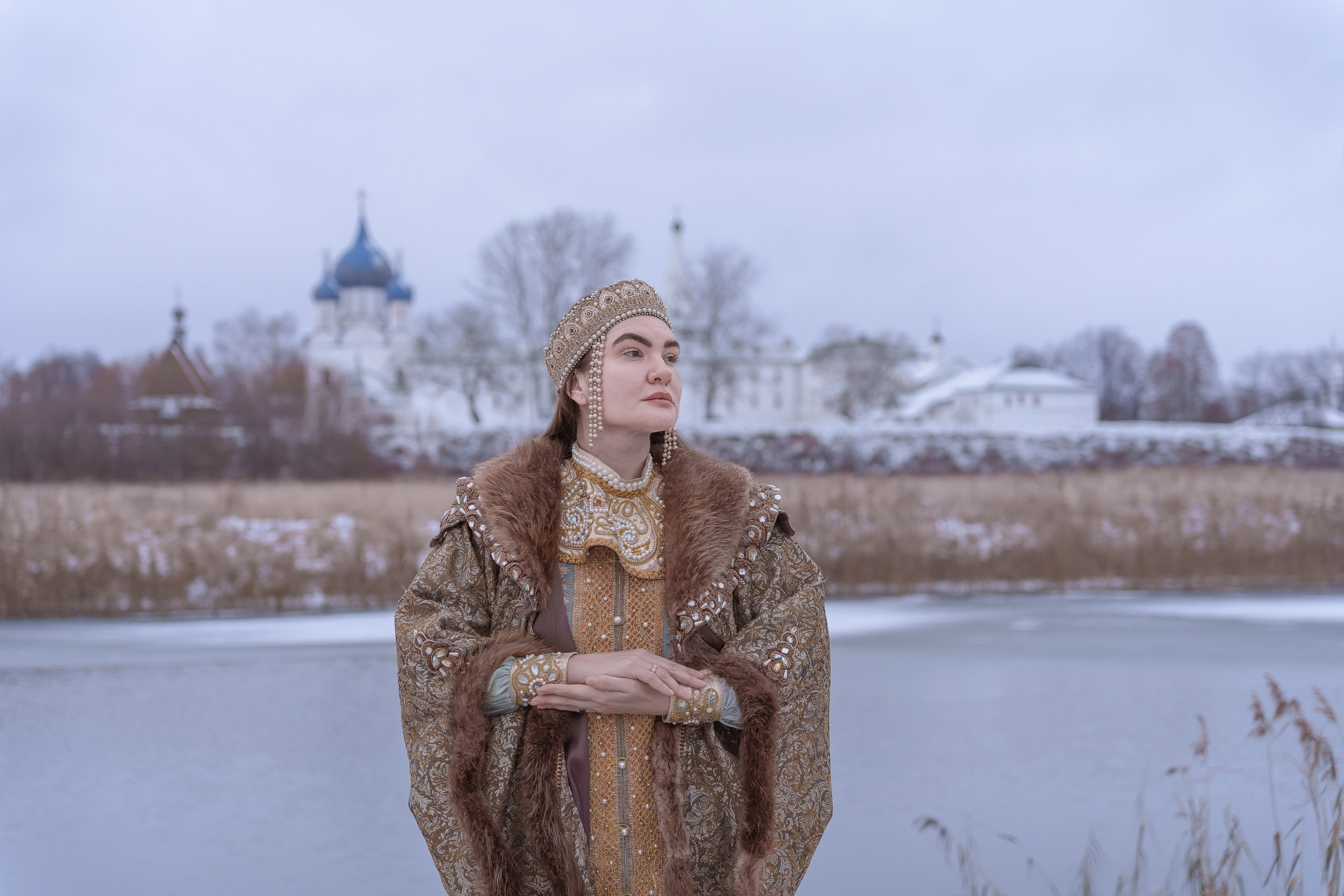 A girl in a boyar costume on the background of a temple in Suzdal by the river