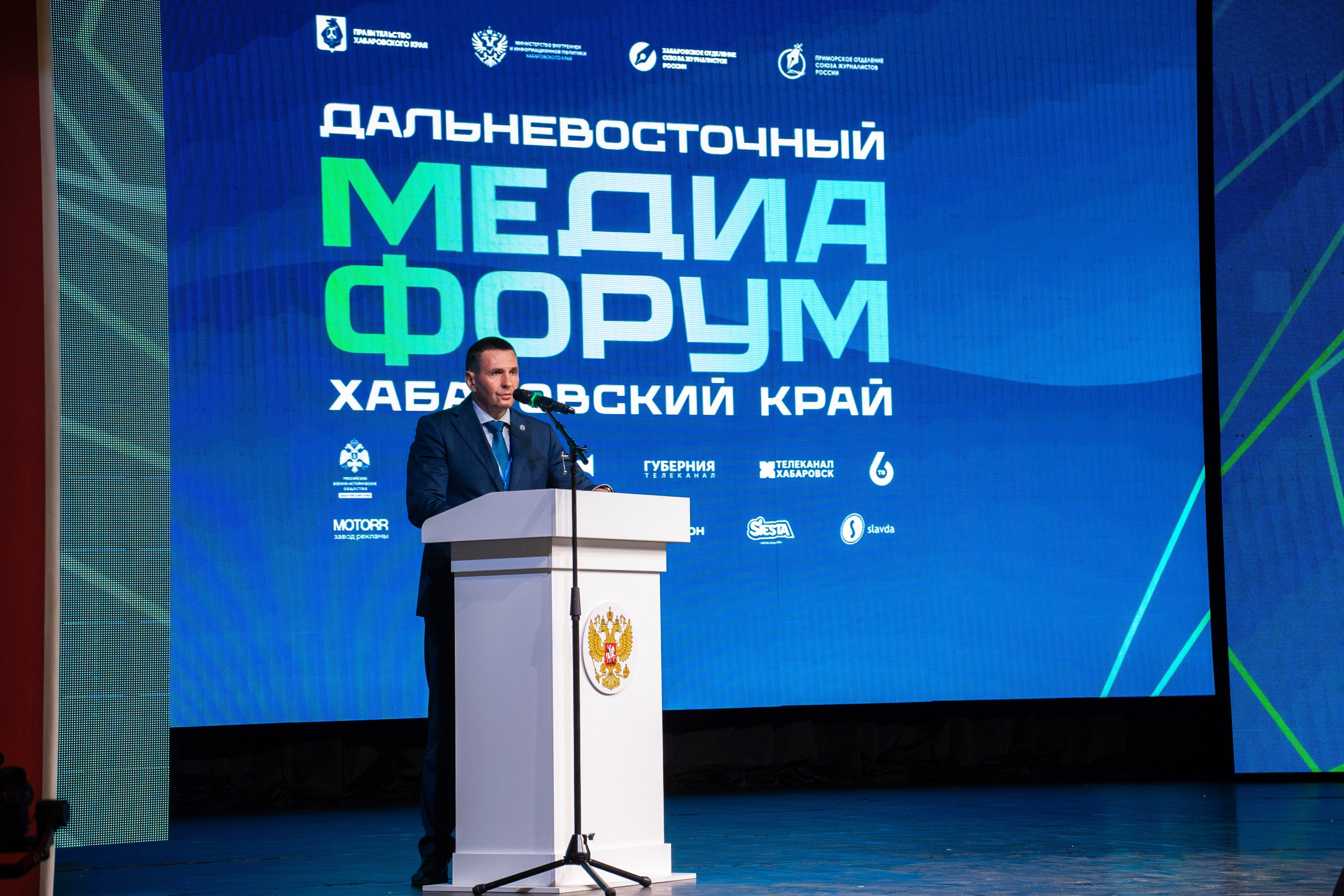 Официальный докладчик на трибуне заснят репортажным фотографом в Хабаровске Дмитрием Дергачевым на фоне синего экрана Дальневосточного медиафорума. Профессиональная съемка мероприятий фотографом в Хабаровске.