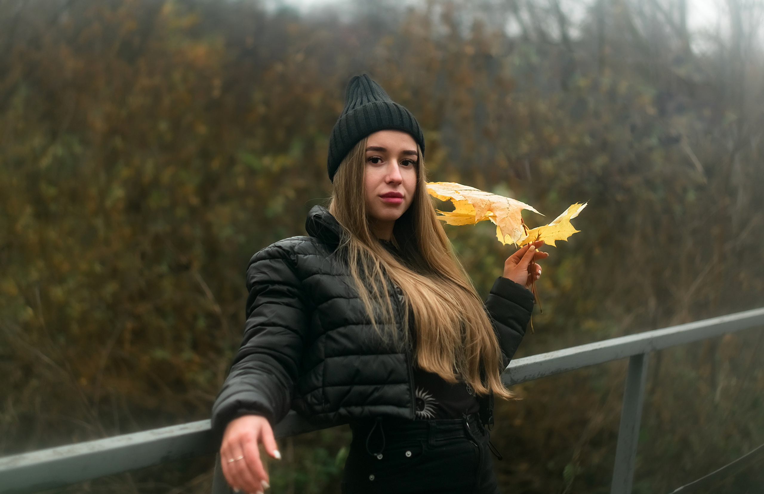 На фото девушка на мостике смотрит вперед и держит в руках осенние листья.