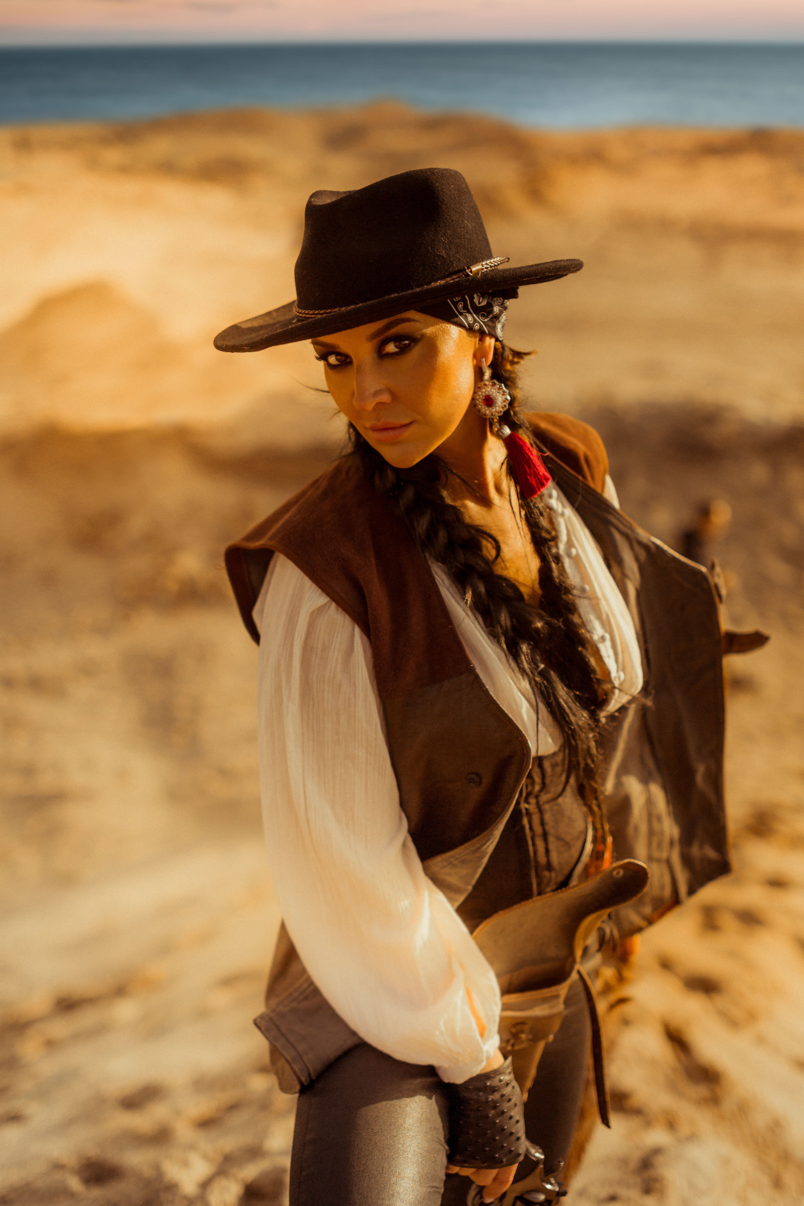 Девушка ковбой с револьвером вестерн на сидит смотрит вдаль в пустыне.