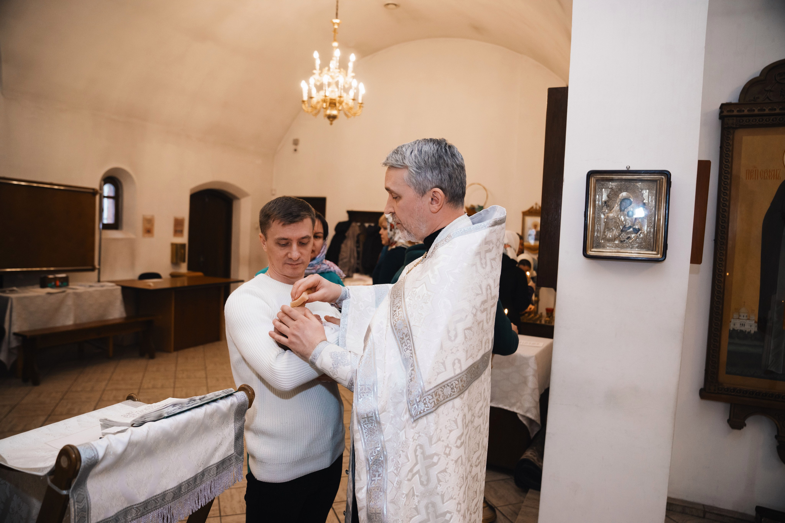 священник держит младенца во время крещения ребенка