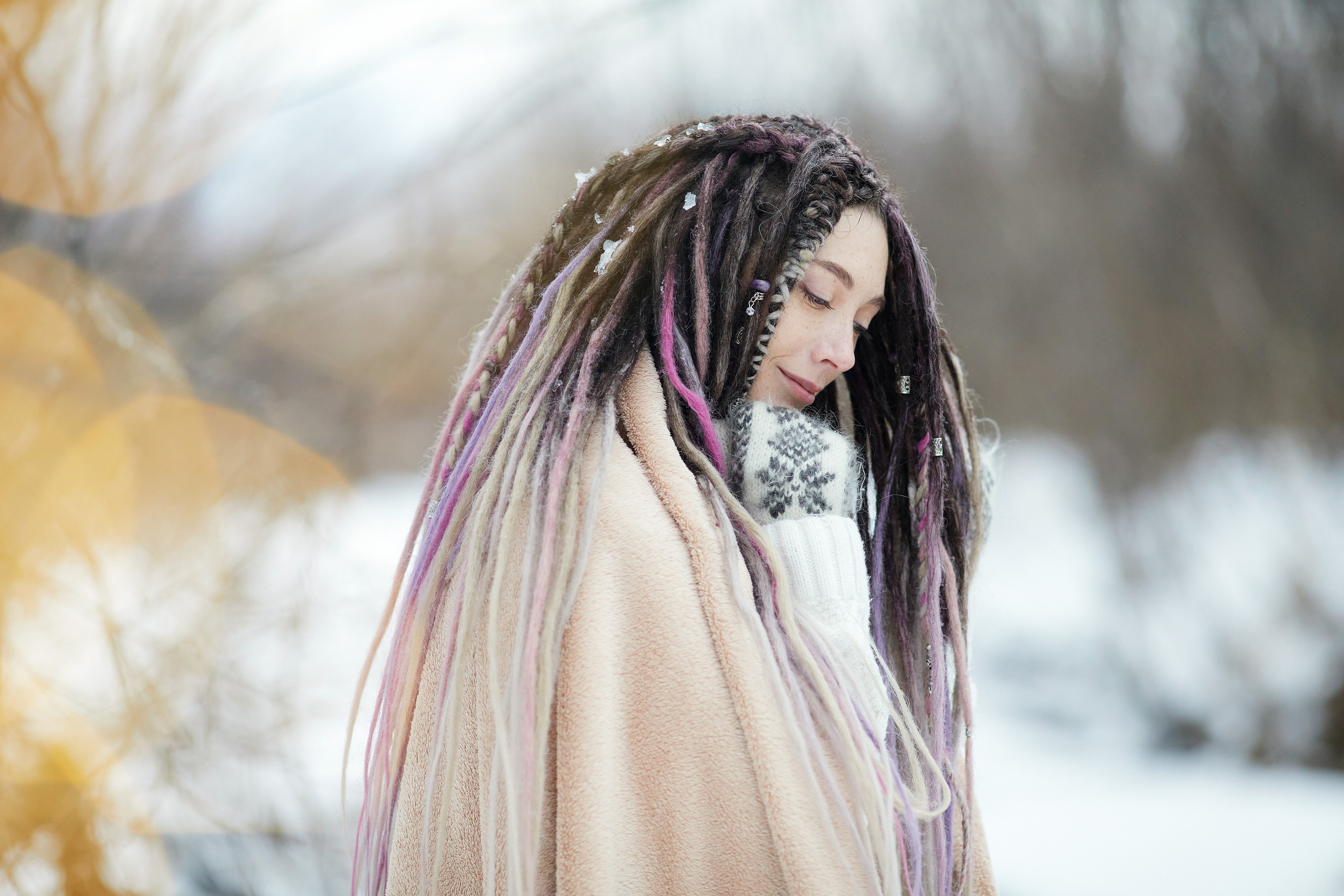 Застенчивая девушка с дредами позирует на фоне размытого зимнего леса
