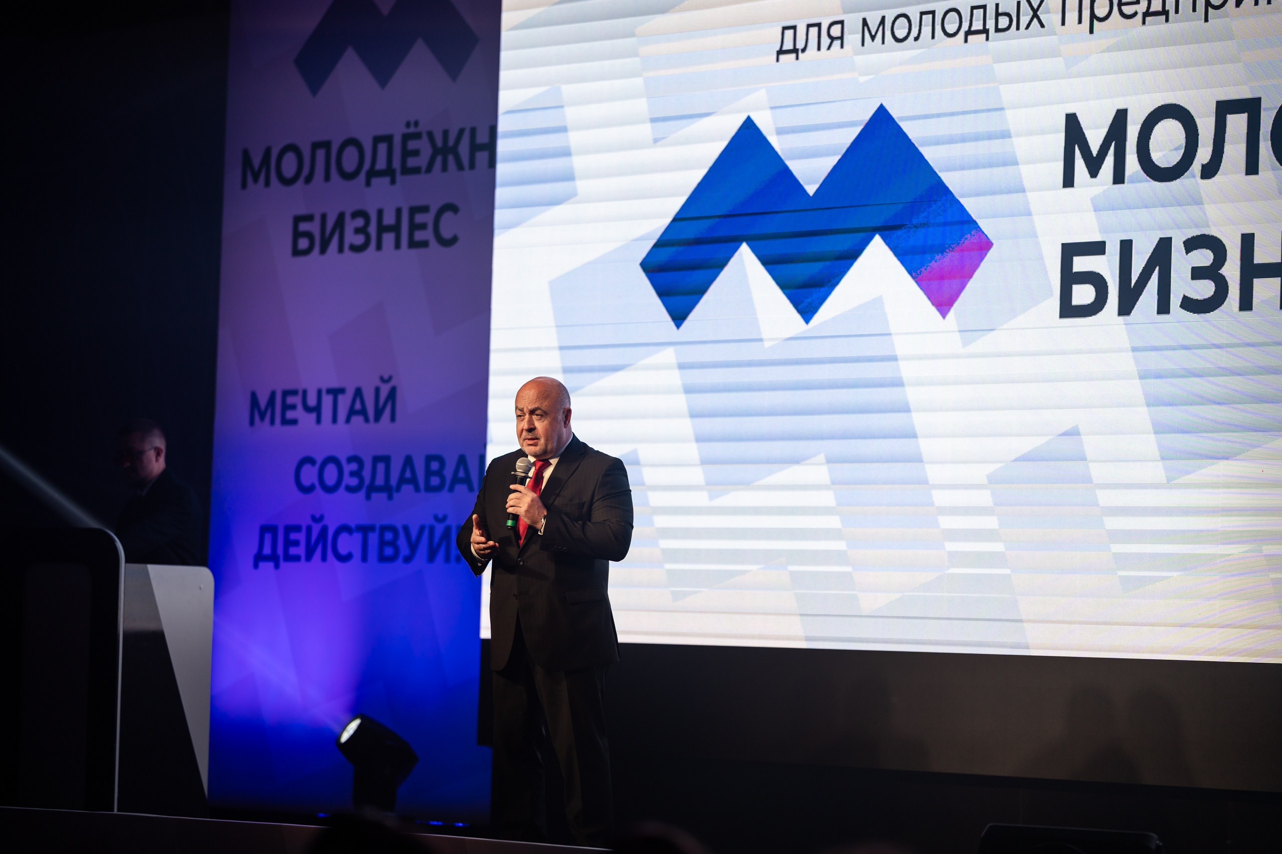 Репортажная съемка форума: Павел Солодкий, Уполномоченный по защите прав предпринимателей в Нижегородской области, выступает с микрофоном на сцене, баннер «Молодёжный бизнес»