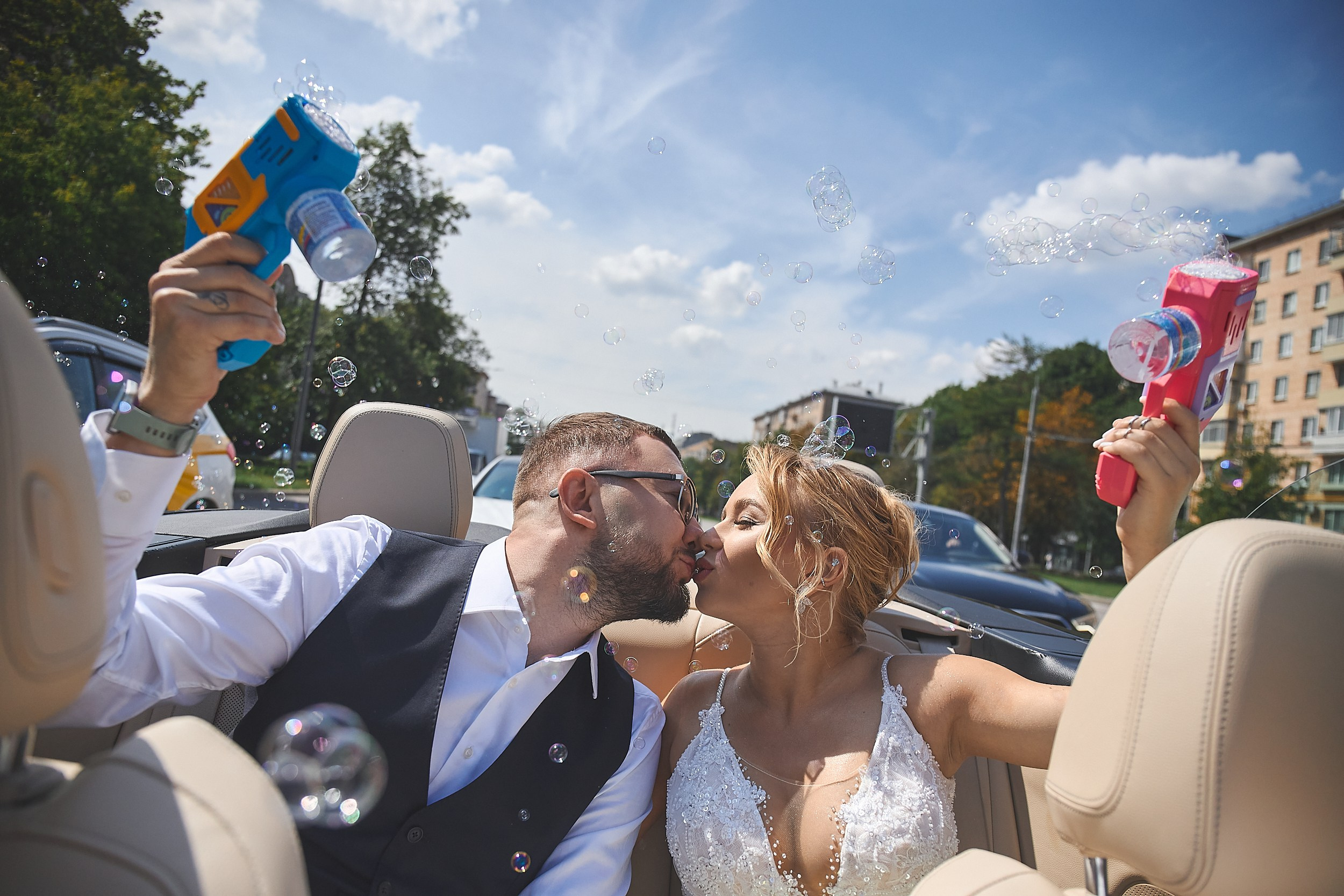 Свадебная пара пускает мыльные пузыри в кабриолете.