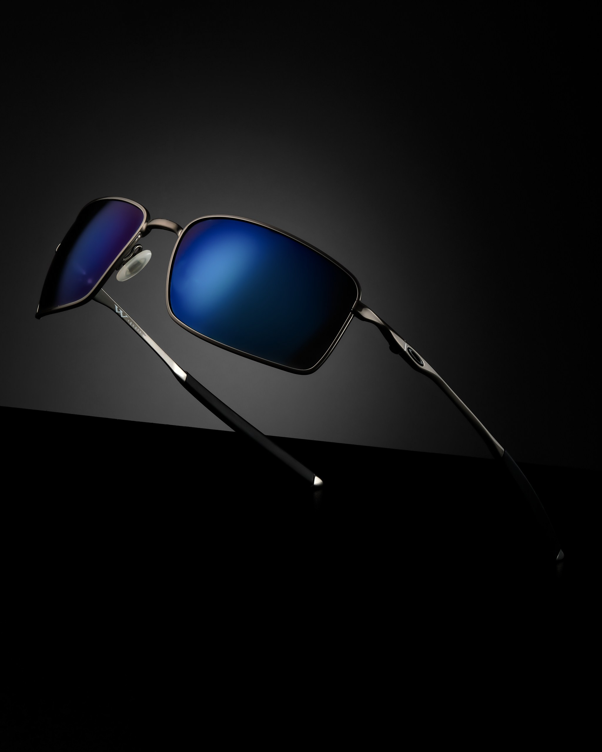 Солнцезащитные очки с синей линзой на тёмном фоне с акцентом на форму и отражение — рекламная съёмка очков для бренда