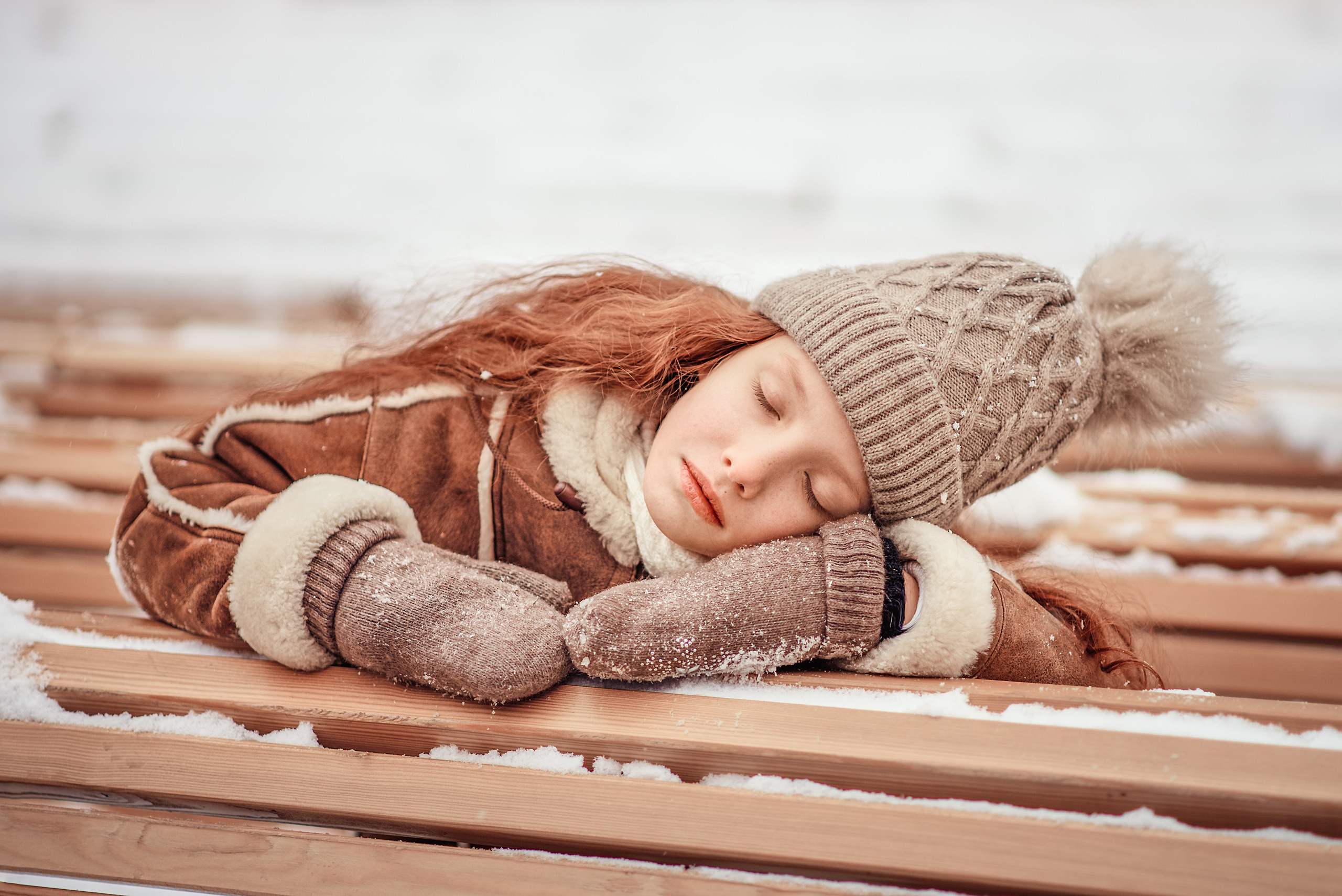 Девочка уснула на скамейке в зимнем парке.