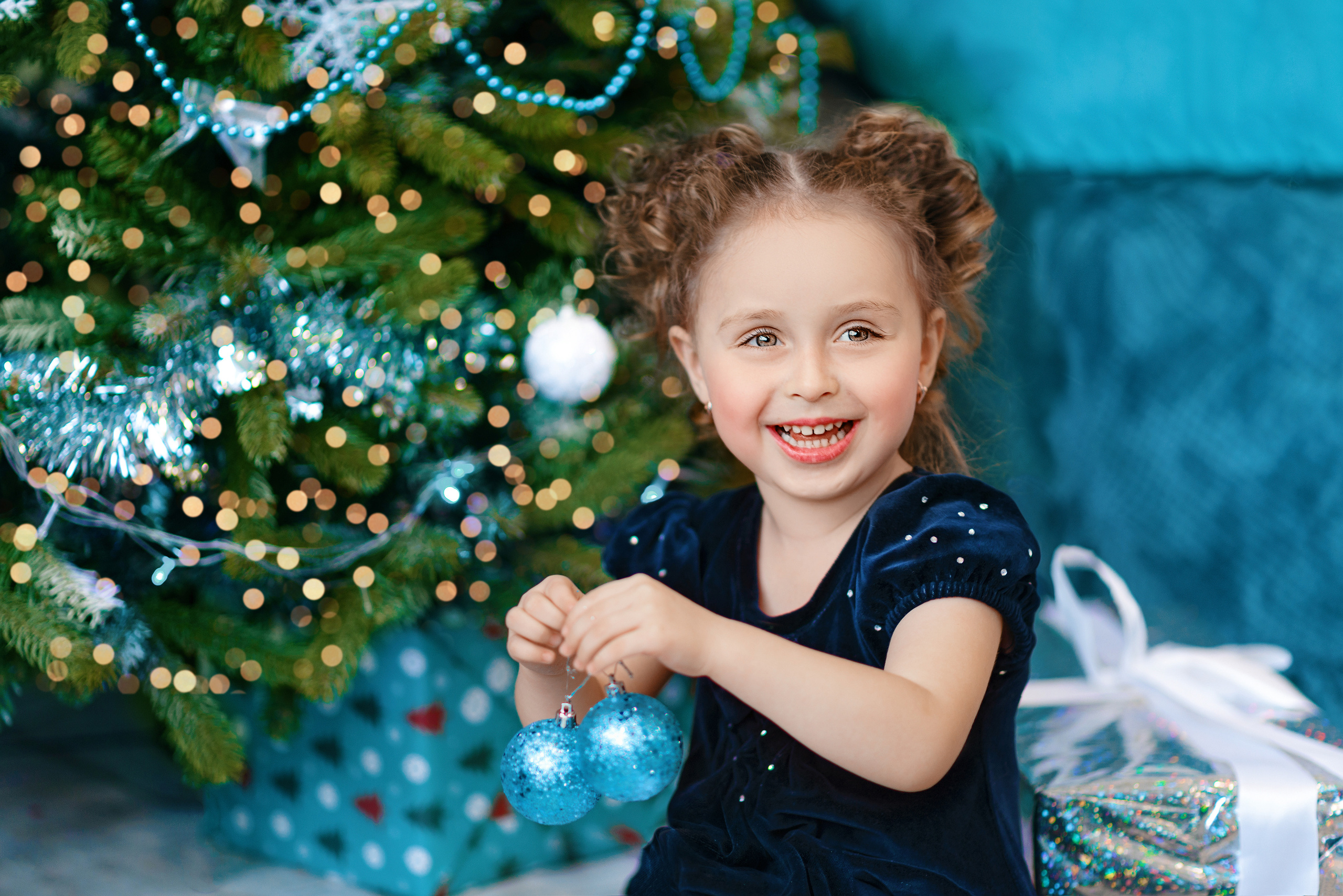 Девочка возле новогодней ёлки держит в руках два новогодних шара.