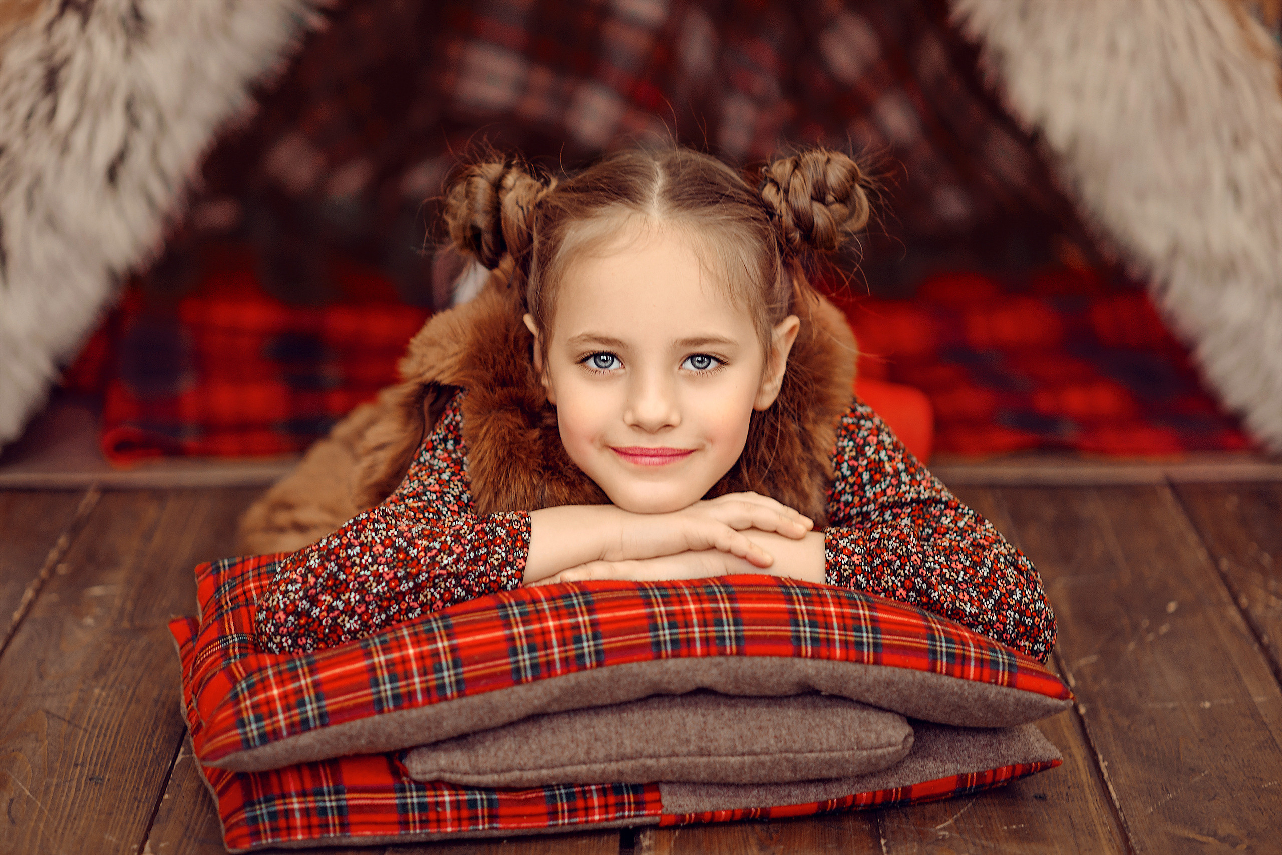 Девочка лежит на полу на красных клетчатых подушках, положив подбородок на руки.