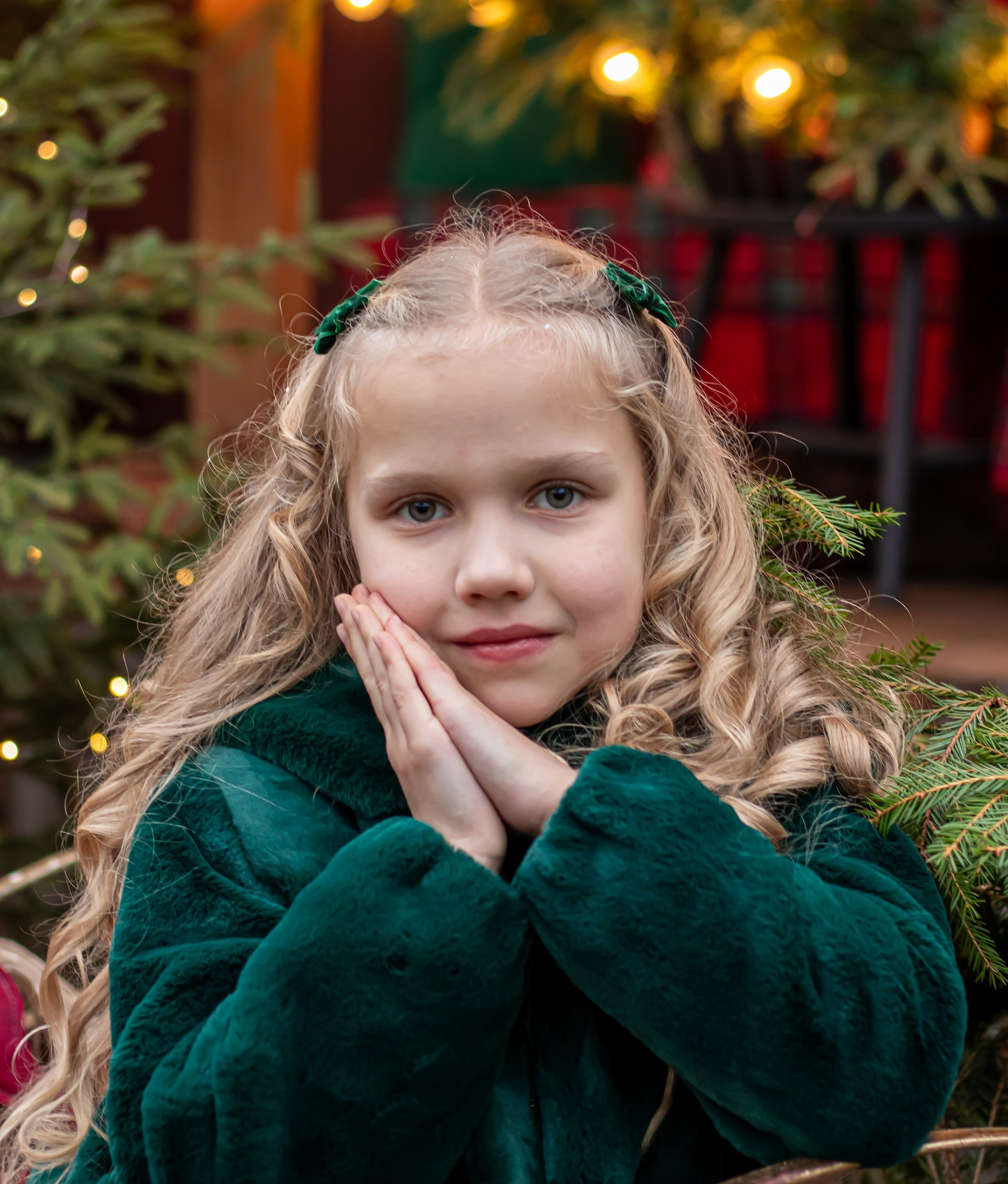 Девочка в зелёной шубке сидит на новогодней фотозоне с ёлками и подарками, фотограф Карасёва Елена