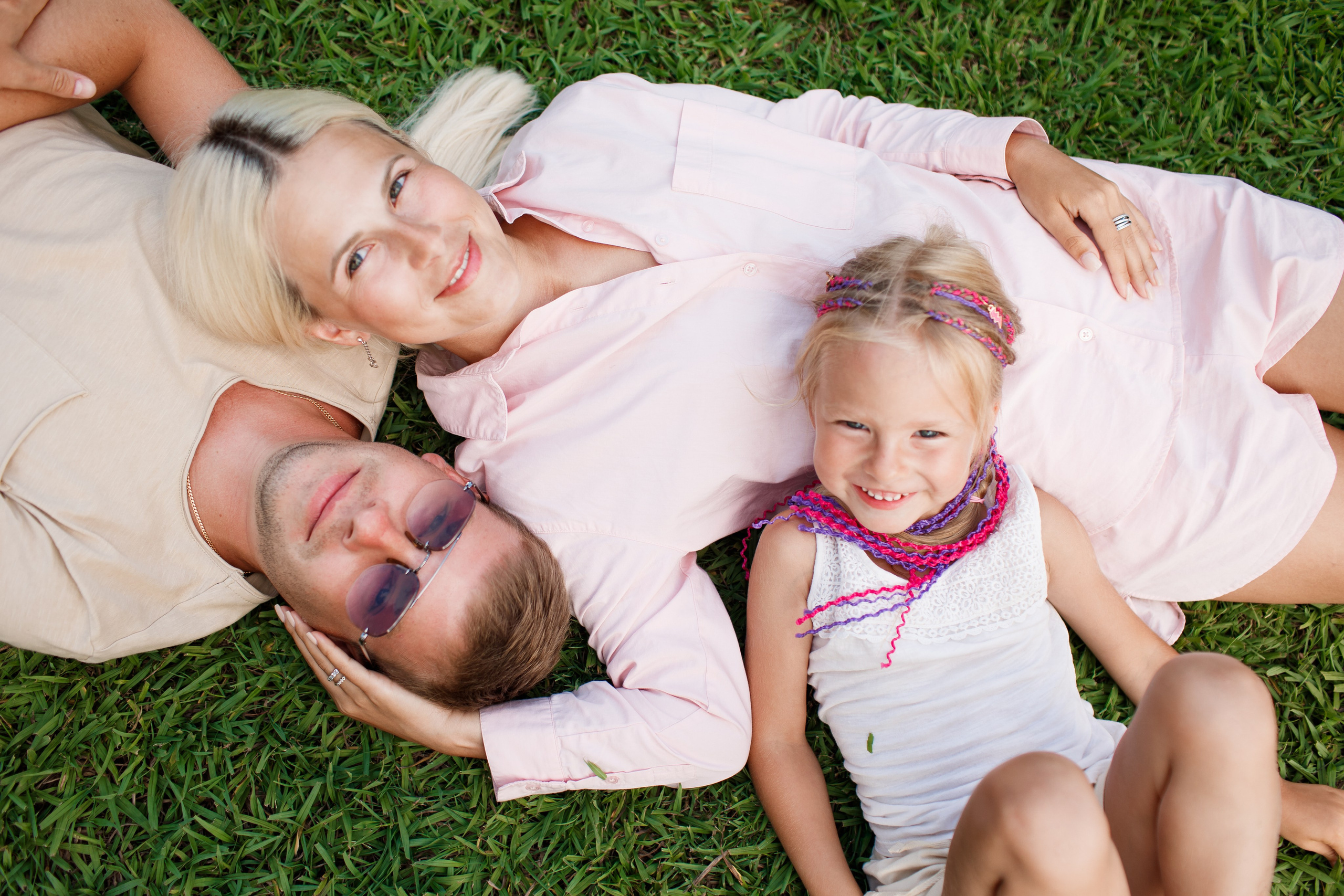 Семья из трёх человек лежит на зелёной траве вместе и смотрит в камеру с улыбкой