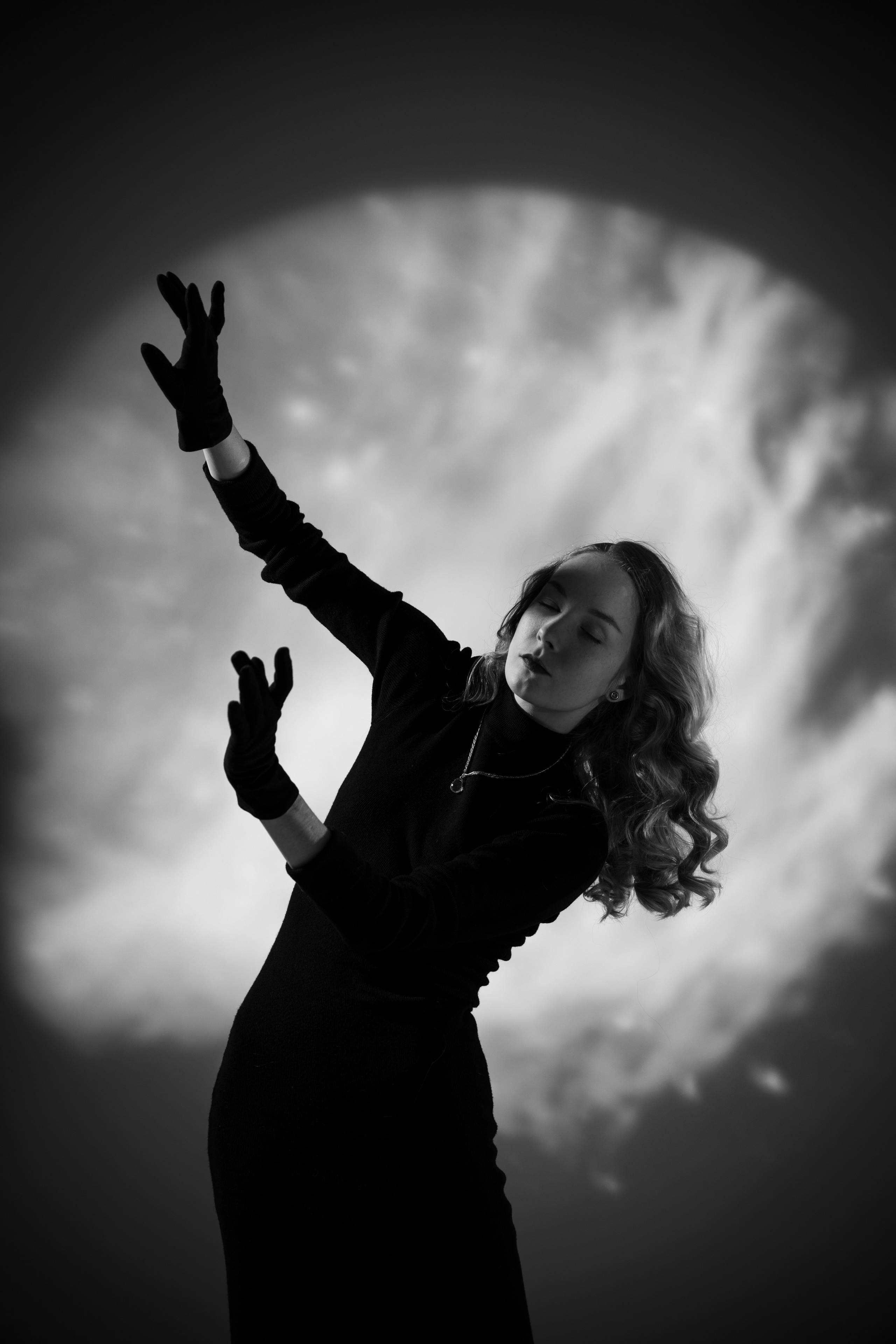 Динамичная студийная фотография девушки с длинными волосами в черном платье и перчатках