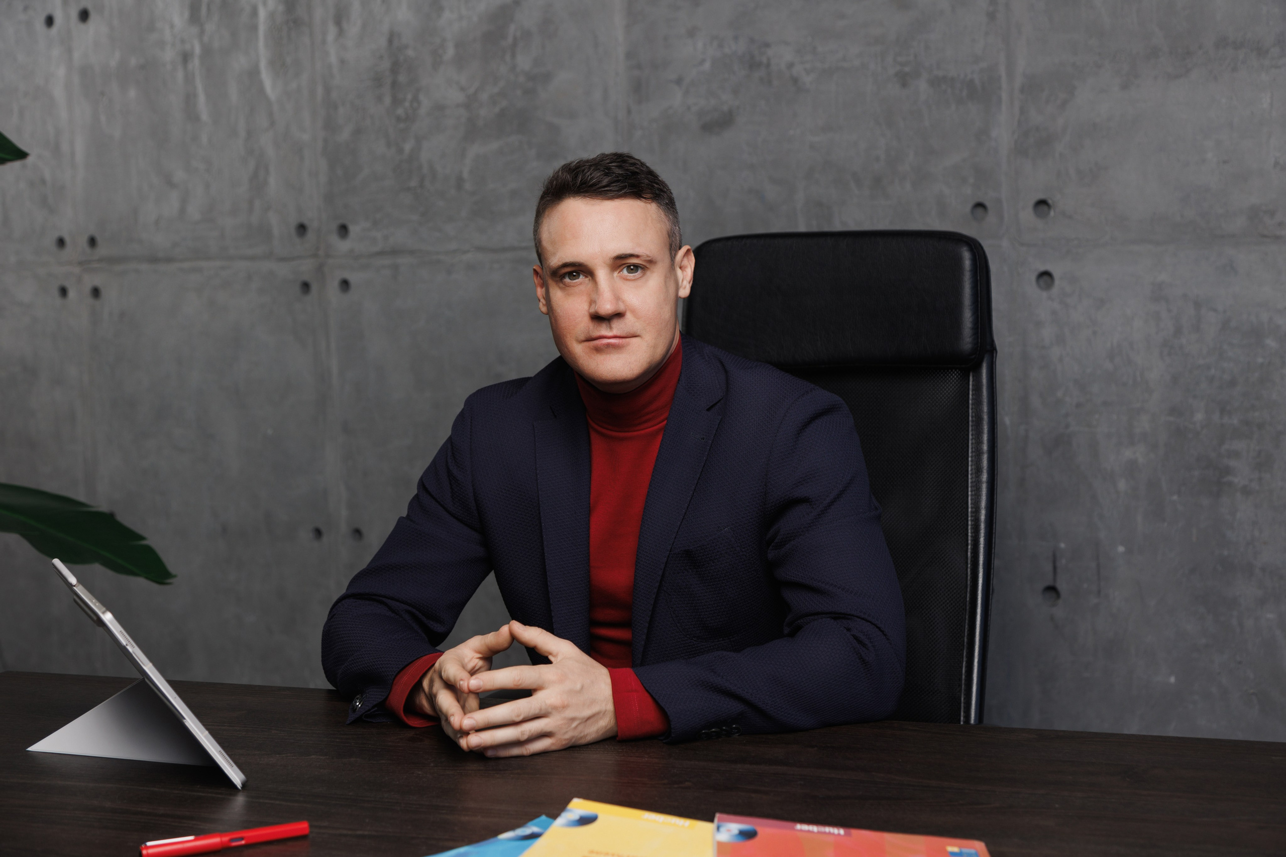 Репетитор сидит за учебным столом, прямо смотря в камеру. Доверительный контакт с потенциальным учеником.