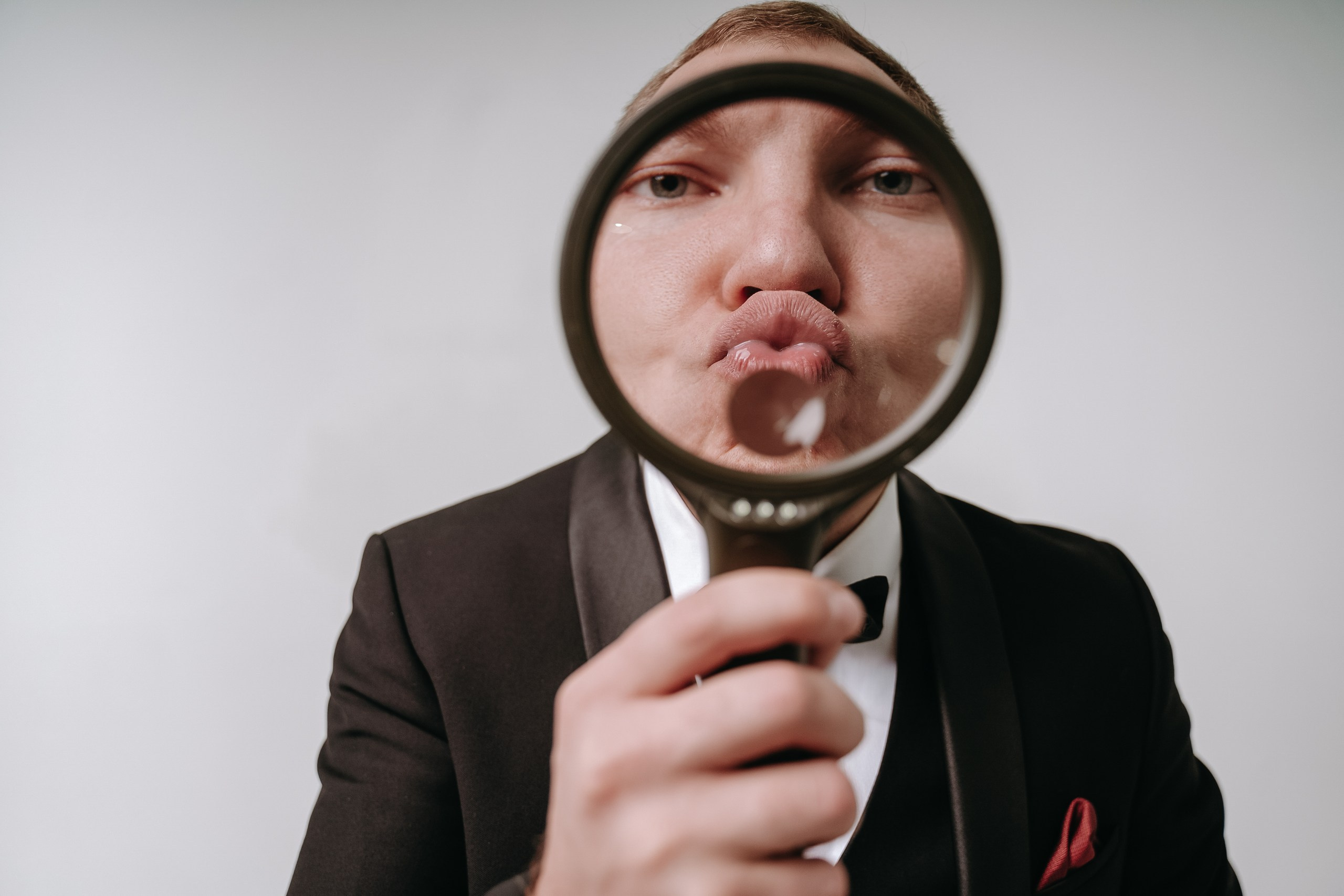 Креативная мужская фотосессия в Уфе: мужчина в смокинге держит увеличительное стекло перед лицом, создавая забавный эффект. Оригинальная съёмка для личного бренда