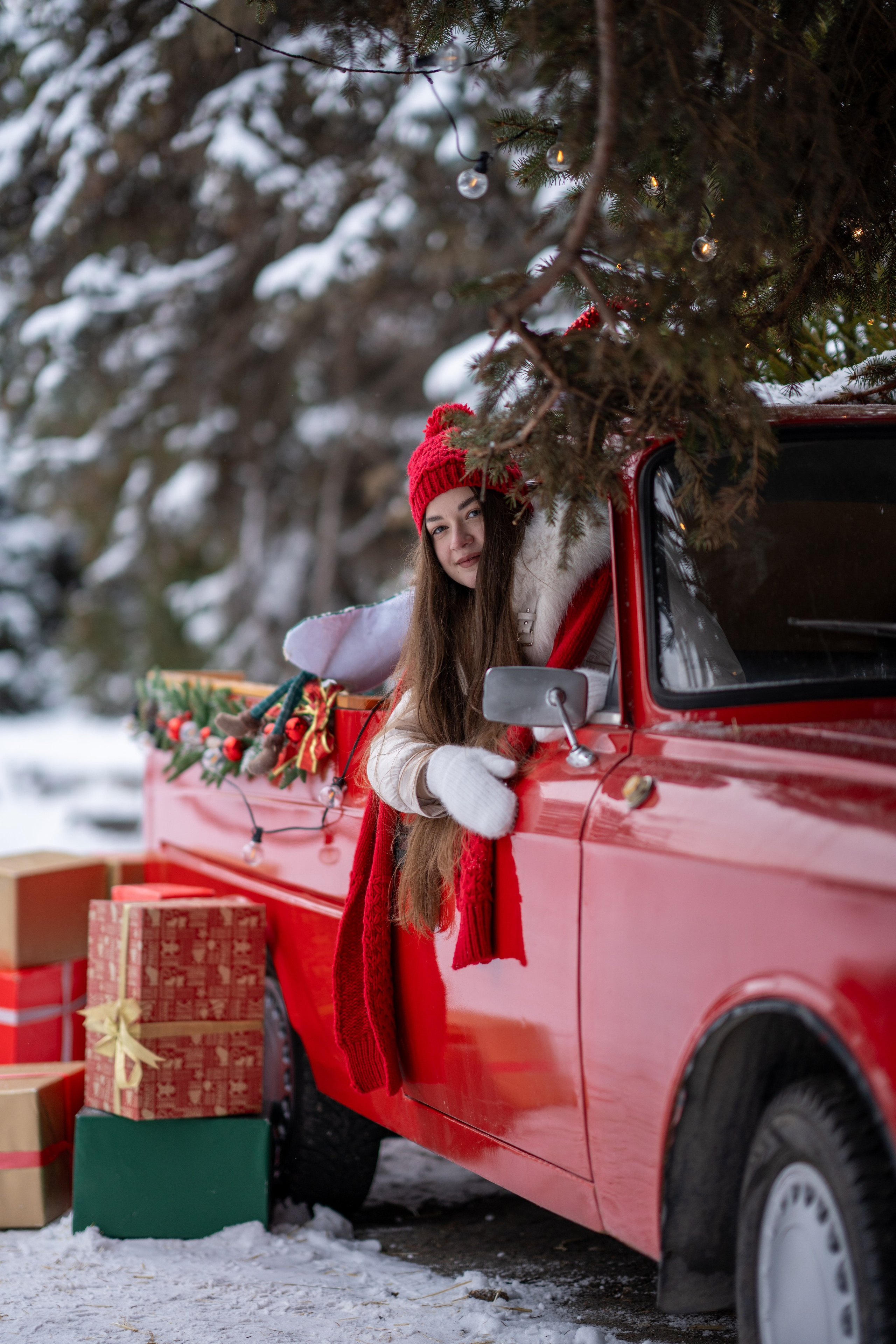 Девушка высовывается из окна красного ретро пикапа с рождественскими декорациями