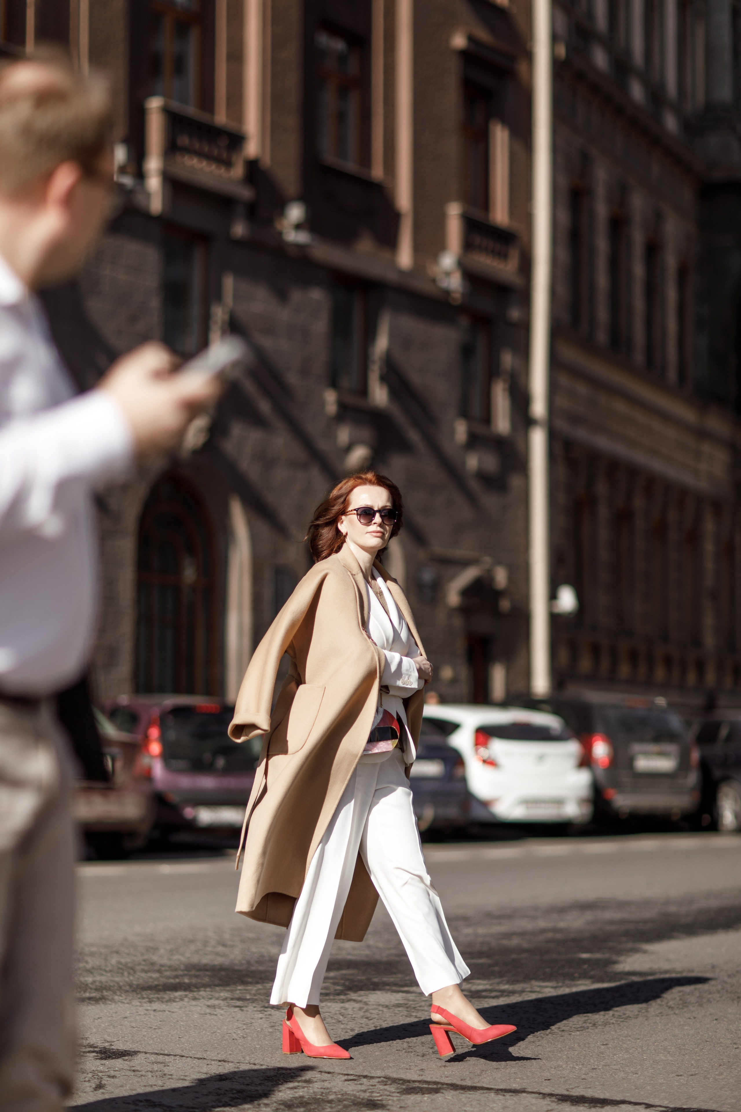 Деловая женщина в бежевом пальто и солнечных очках идет по улице