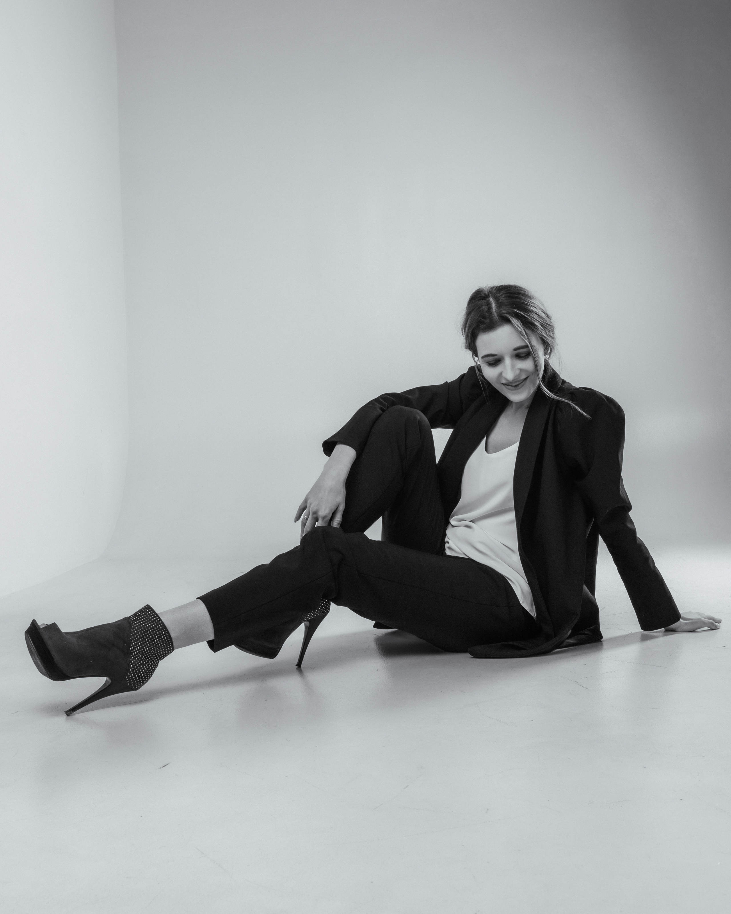 Студийная фотосъёмка девушка в пиджаке сидит на белой циклораме