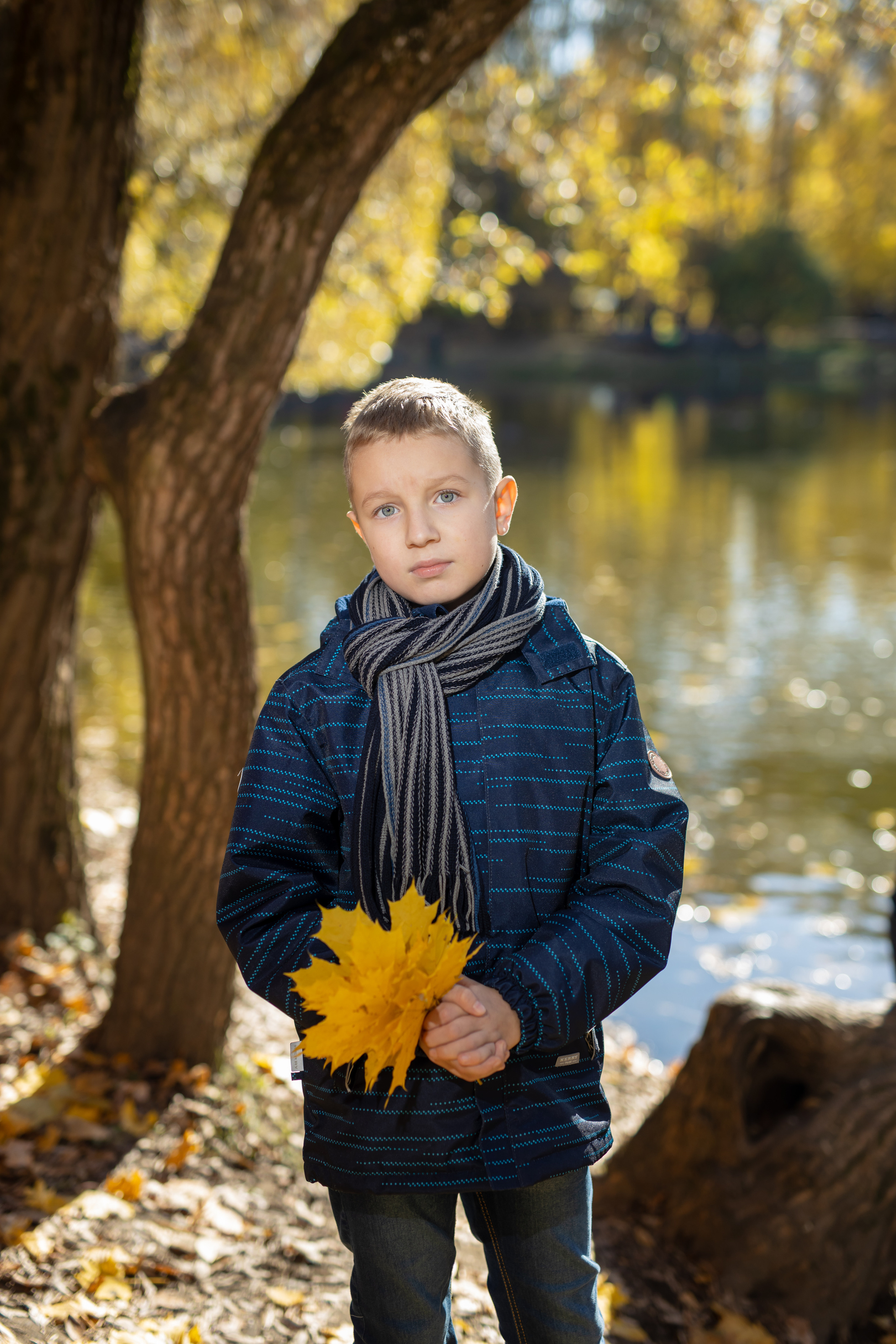 Мальчик в синей куртки и серым шарфом букет из листьев поделки на осень