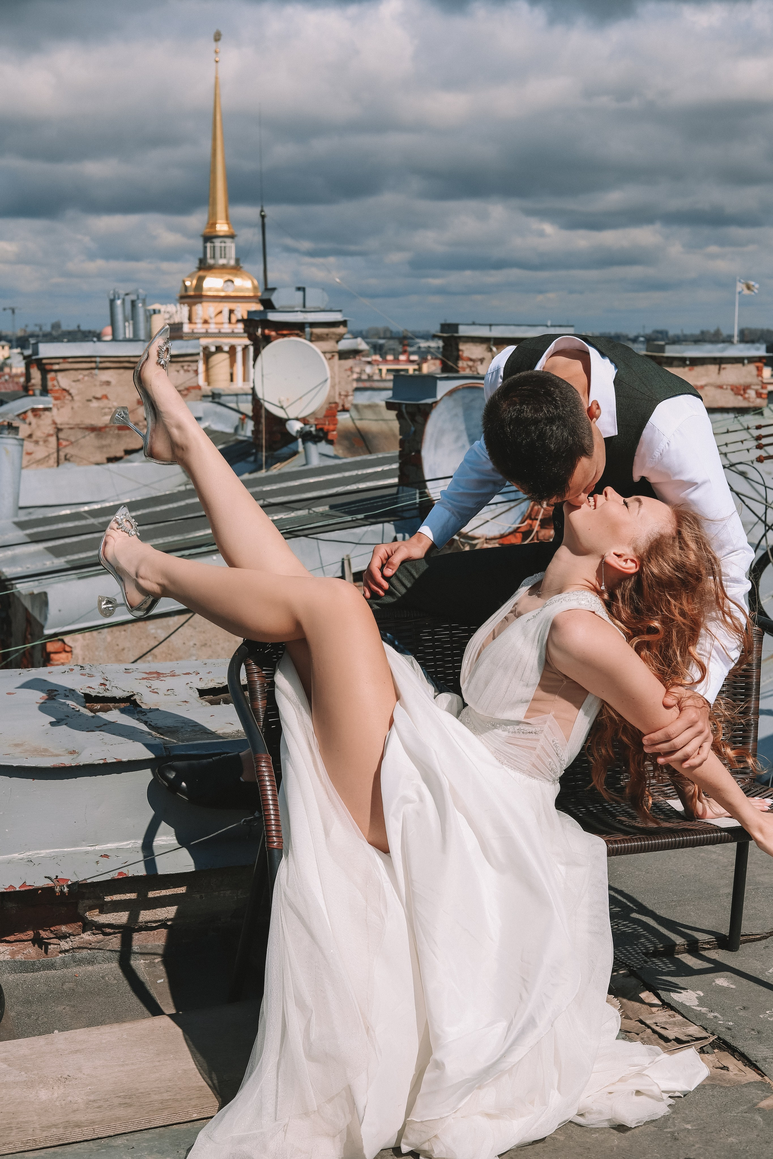 Поцелуй на крыше жениха и невесты, фата развивается, вид на город