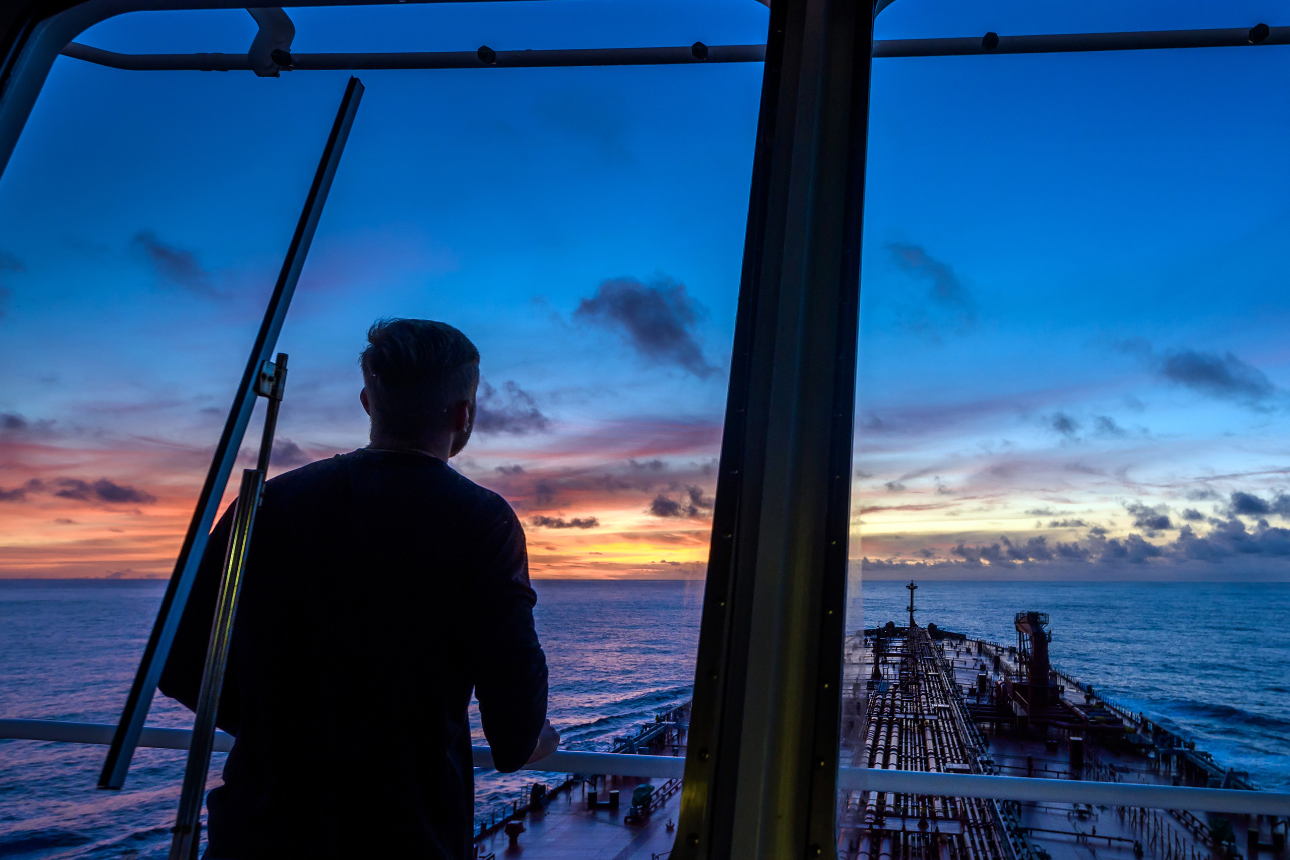 Моряк, наблюдающий закат Солнца на борту танкера