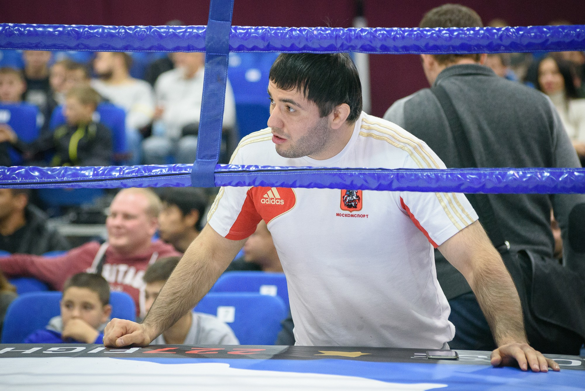 Тренер бойца ММА облокотившись на ринг следит за боем