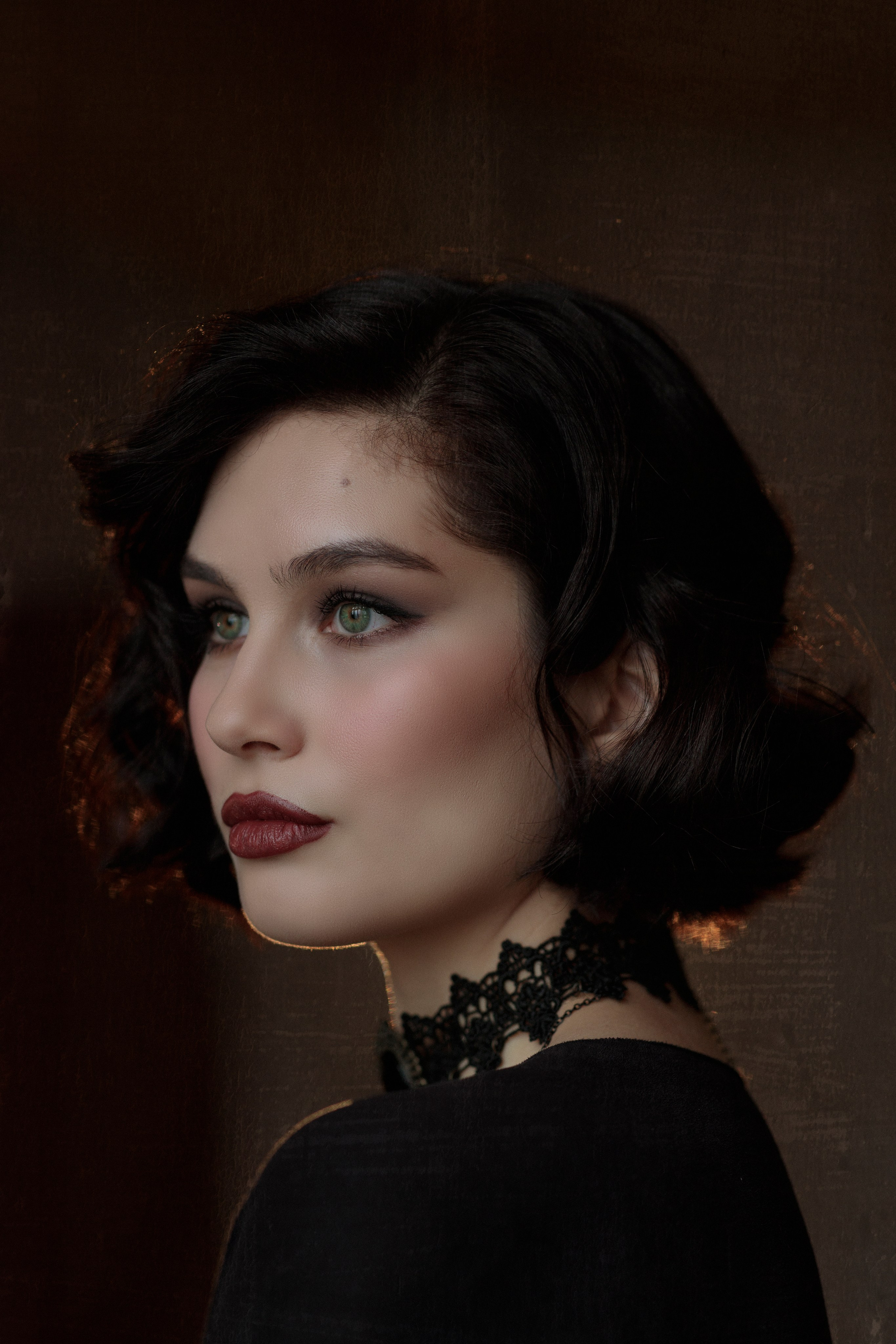 Портрет девушки в профиль, глаза ярко-зелёного цвета, тёмные волосы и губы накрашены ярко-терракотовой помадой, волосы до плеч, уложены в ретро укладку