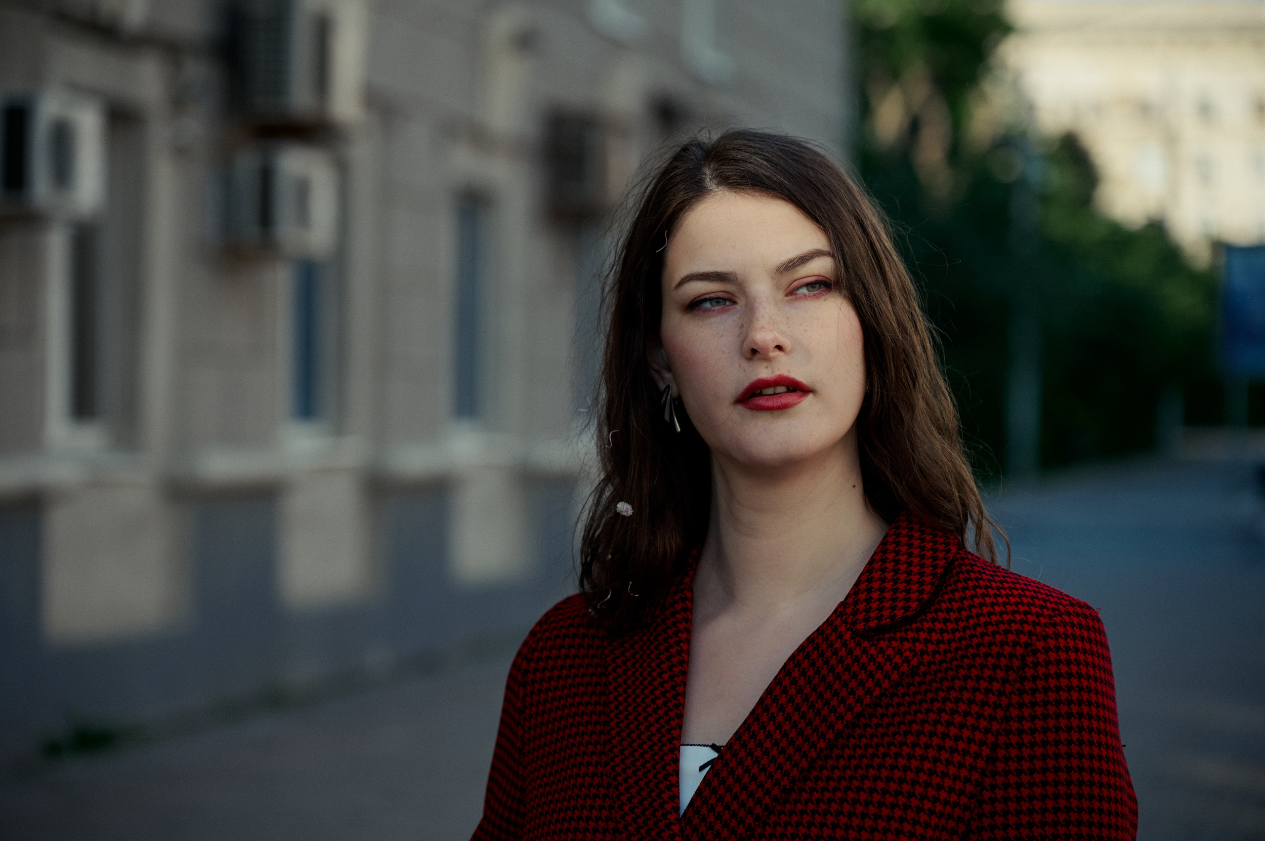 Портрет крупным планом на улице, выразительный взгляд и макияж, деловой образ в бордовом. Фон — городская улица.