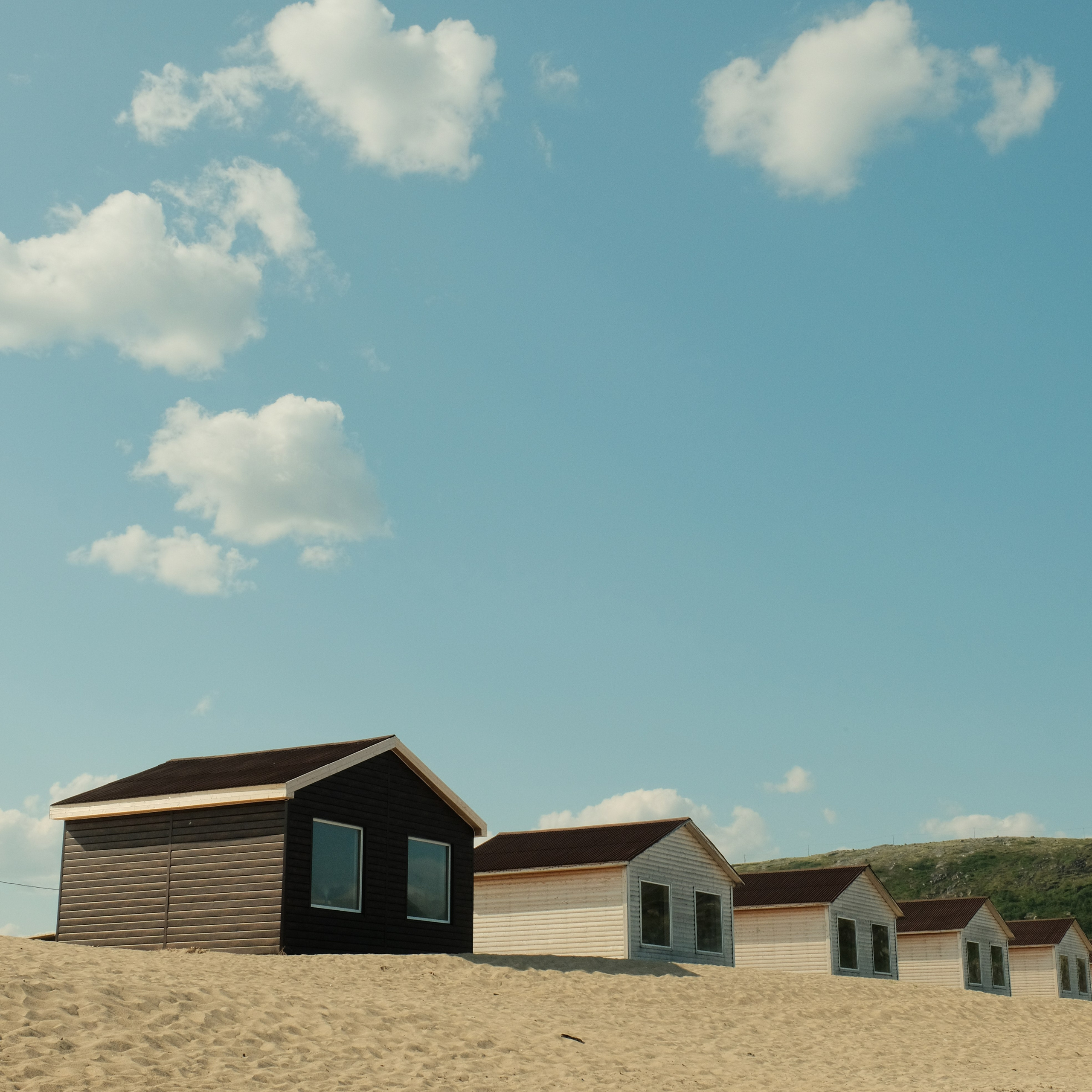 Пять домов стоят в ряд на песке, на берегу Баренцева моря в Териберке, над головой голубое небо.