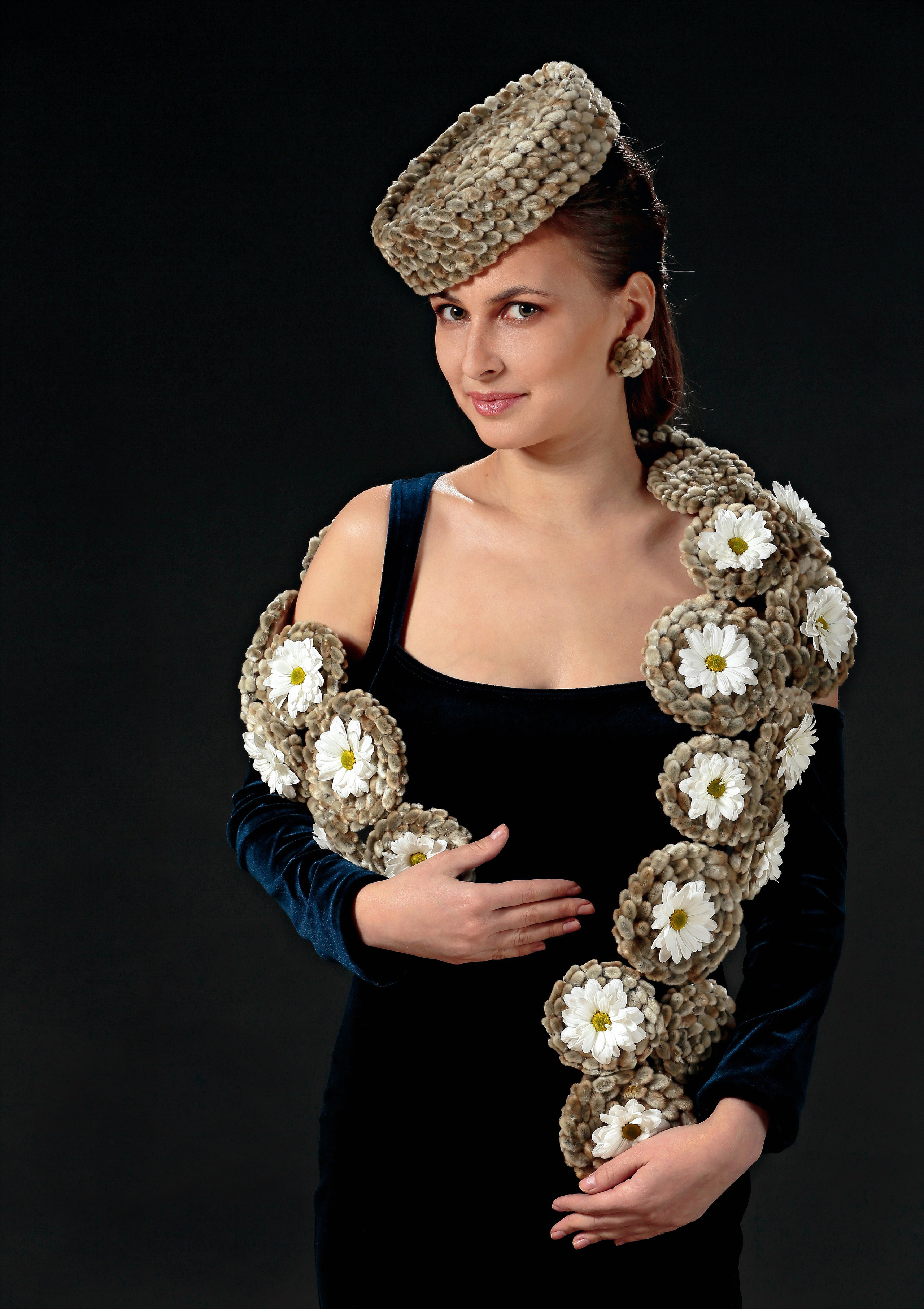 Портрет девушки с шарфом и головным убором из почек ивы и цветов на чёрном фоне.