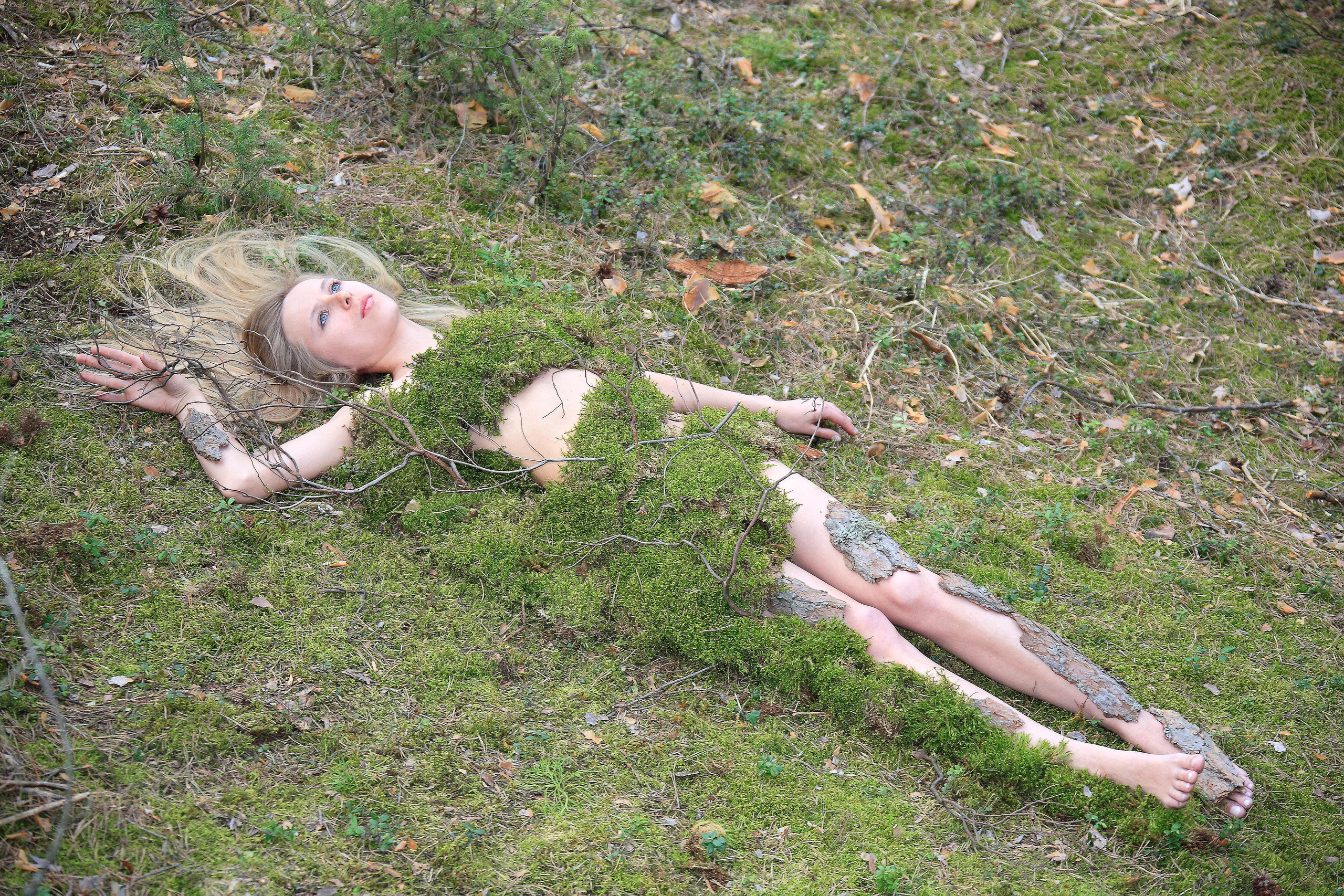 Девушка, украшенная мхом, лежит на земле, покрытой мхом.