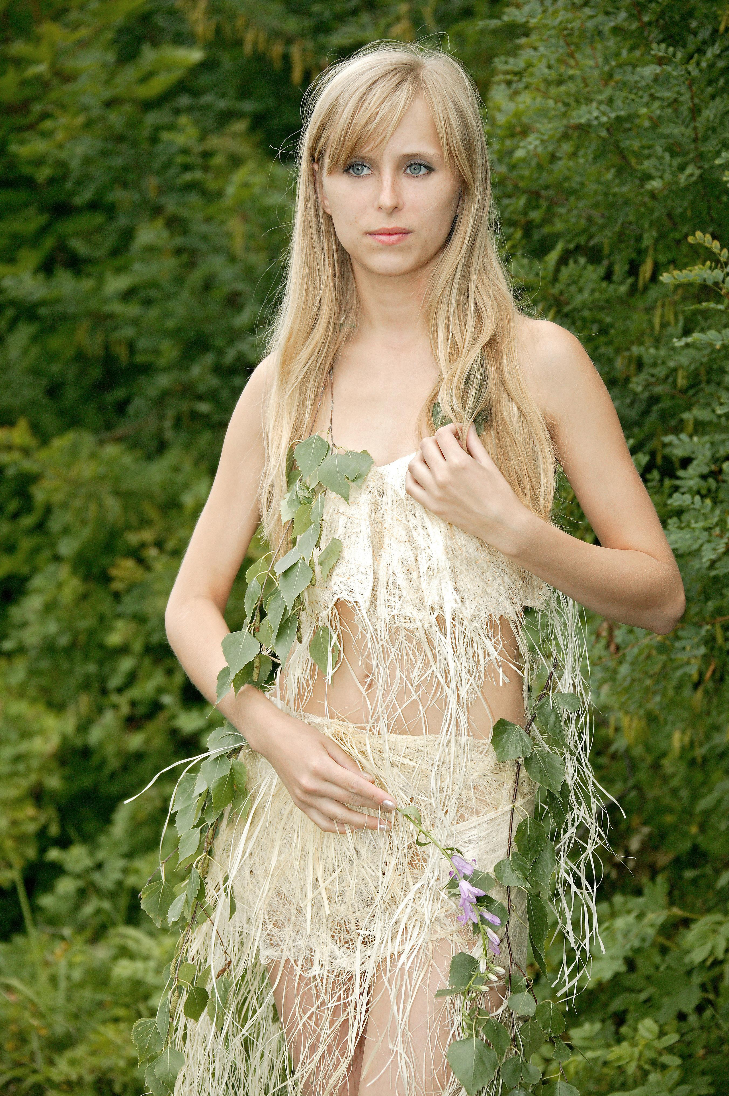 Девушка в топике и юбке из сезали с ветками берёзы на фоне листьев.