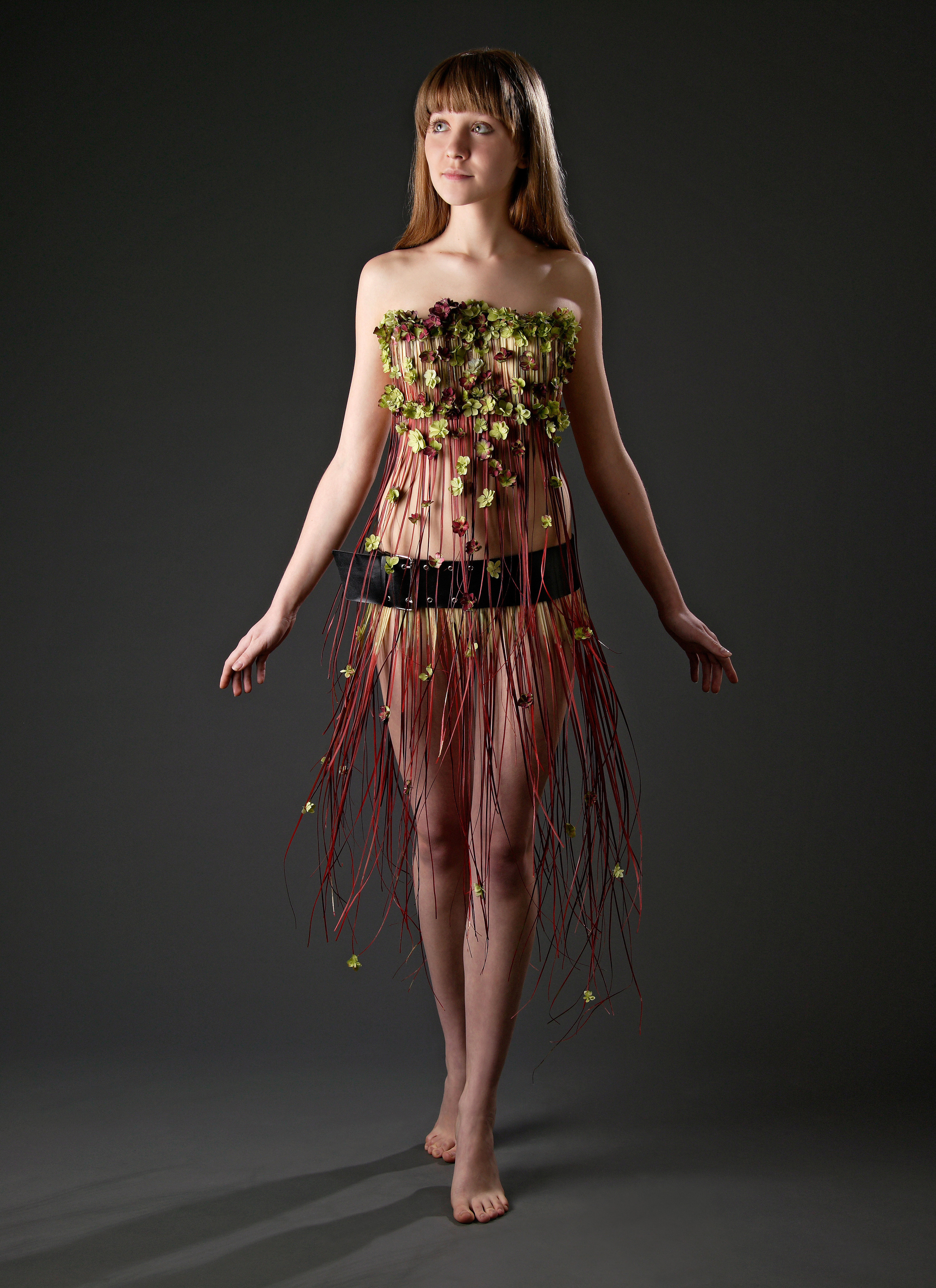 Девушка в платье из тонких длинных красных веточек, украшенных цветами гортензии стоит на чёрном фоне.