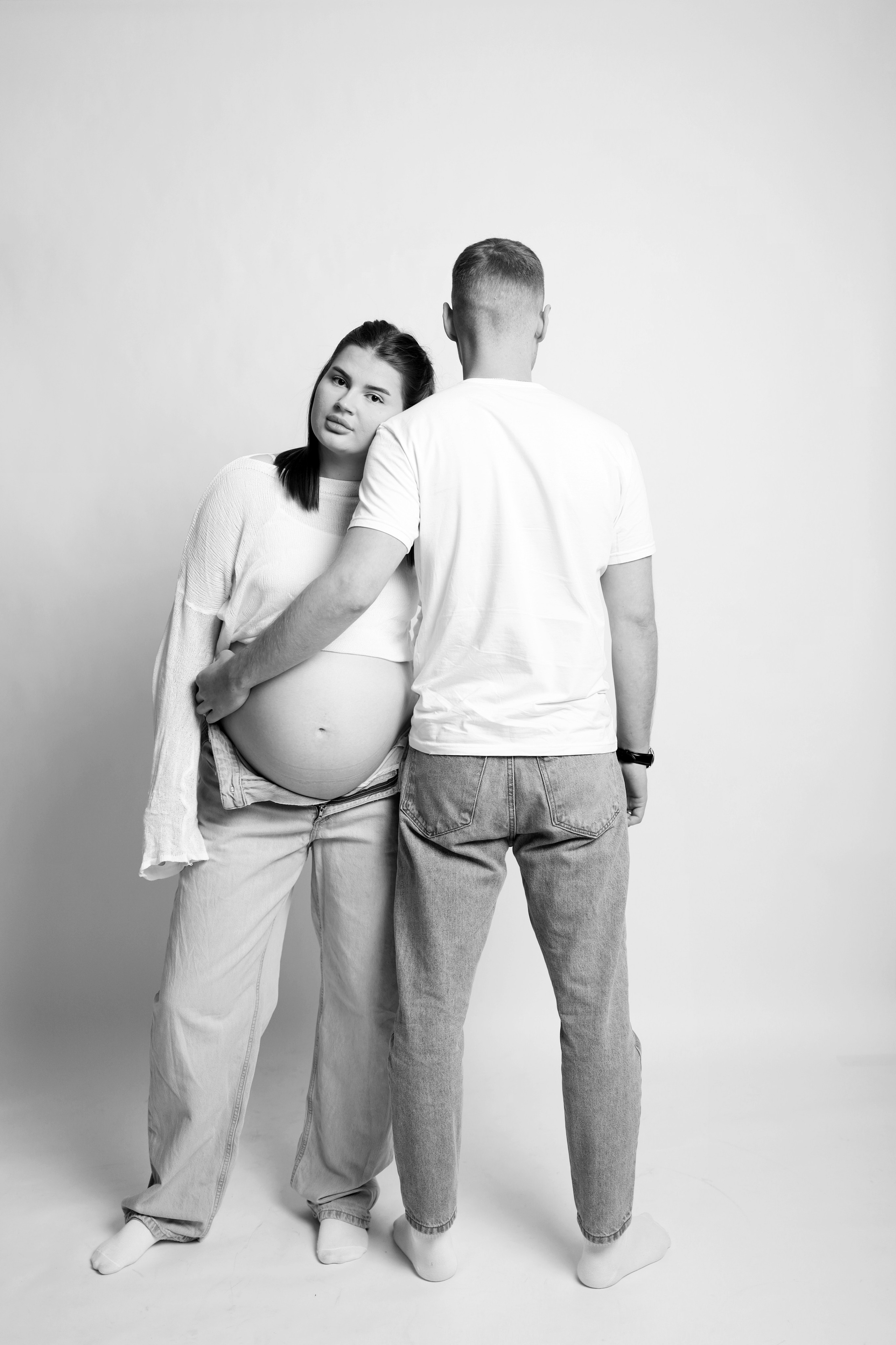 Муж нежно держит живот беременной жены перед камерой фотоаппарата в студии