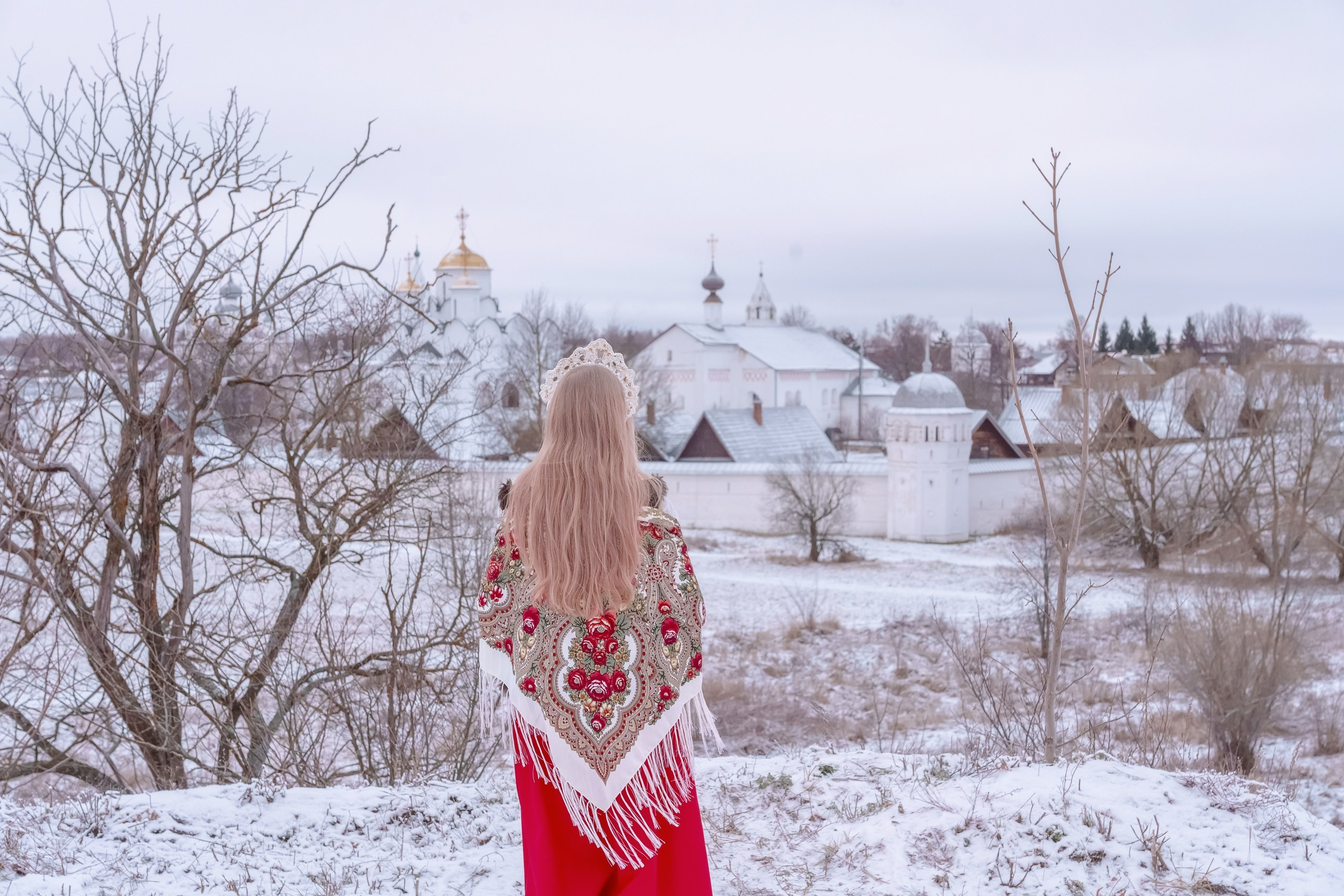 A girl in a Pavlovo Posad shawl and a red skirt on the background of a temple by the river
