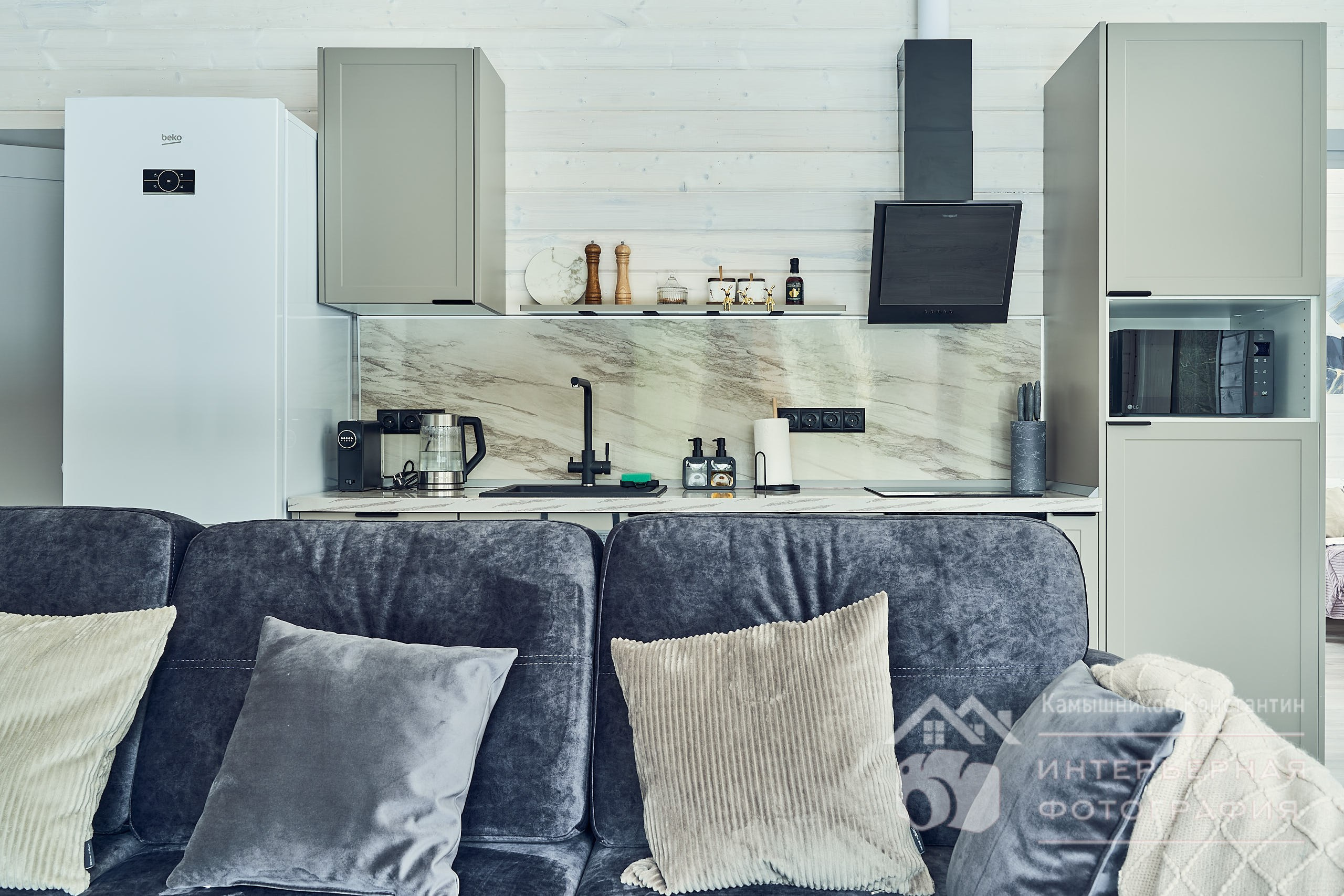 Интерьерная фотография с диваном на переднем плане и кухонной зоной на заднем плане. Всё близко и удобно организовано в загородном доме в Московской области