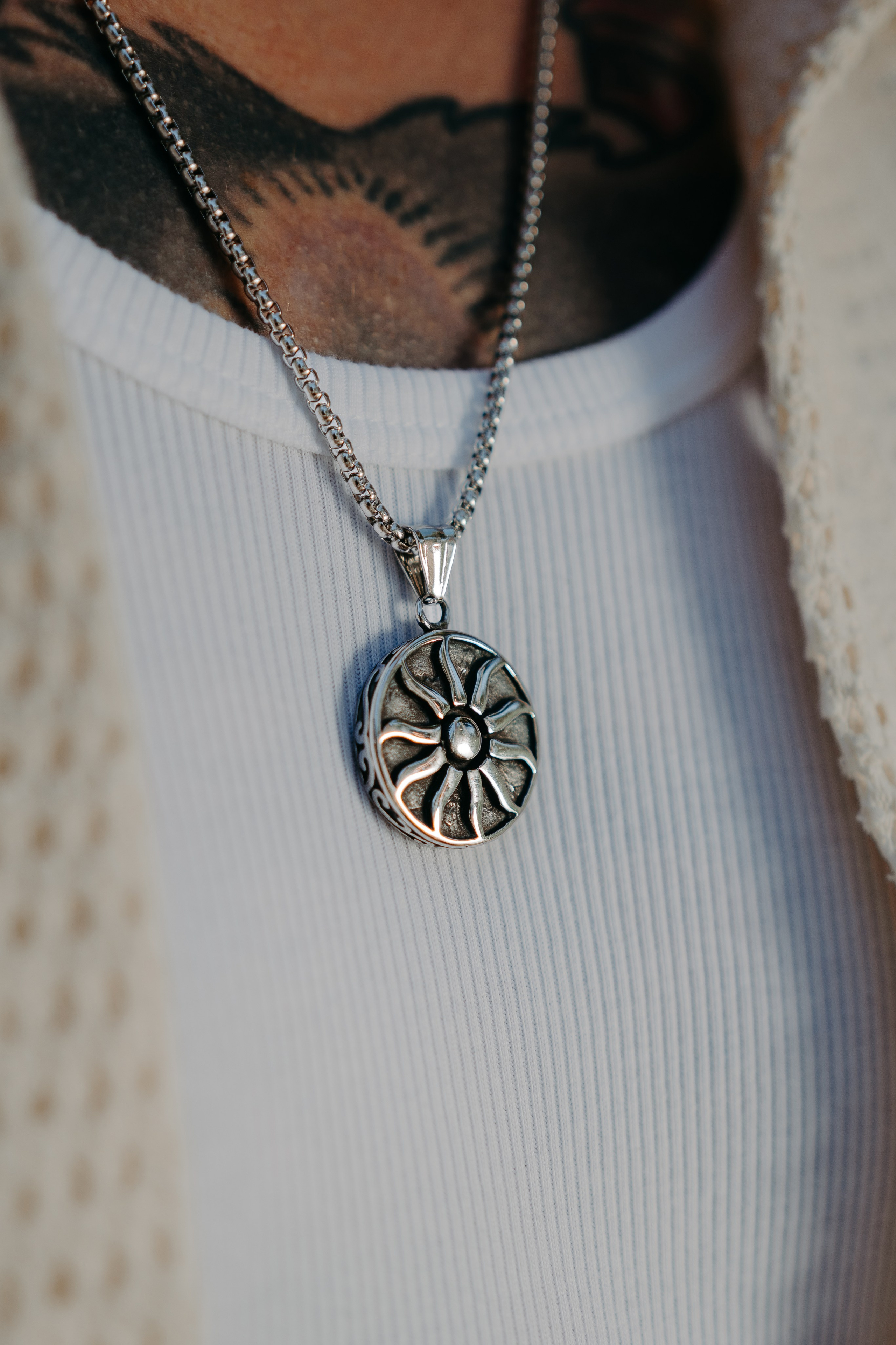 Necklace with a sun-shaped pendant worn over a casual white shirt, representing bohemian style.