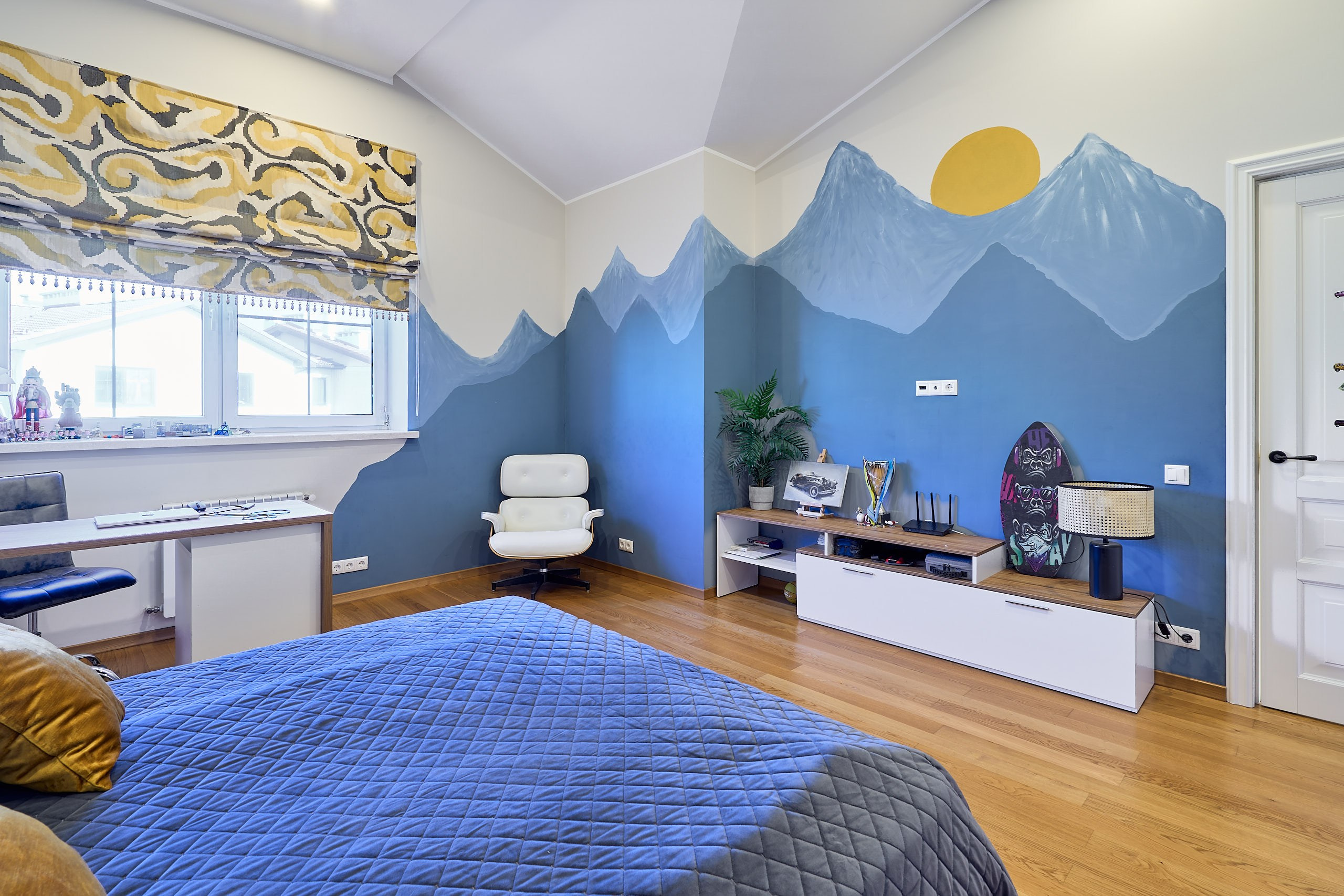 Интерьерная съемка детской с рисунком синих гор на стене и синим покрывалом на постели