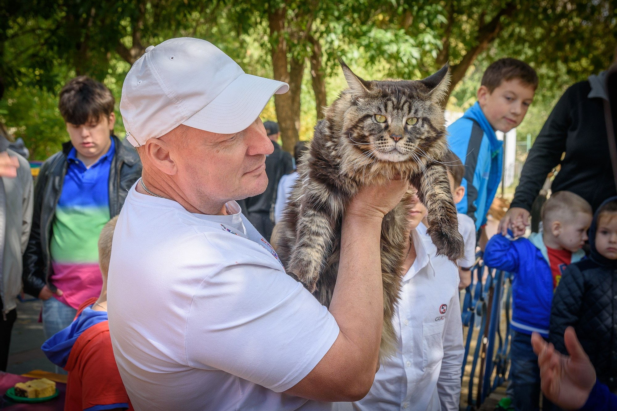 Мужчина в белой кепке держит в руках большого кота мейн-куна