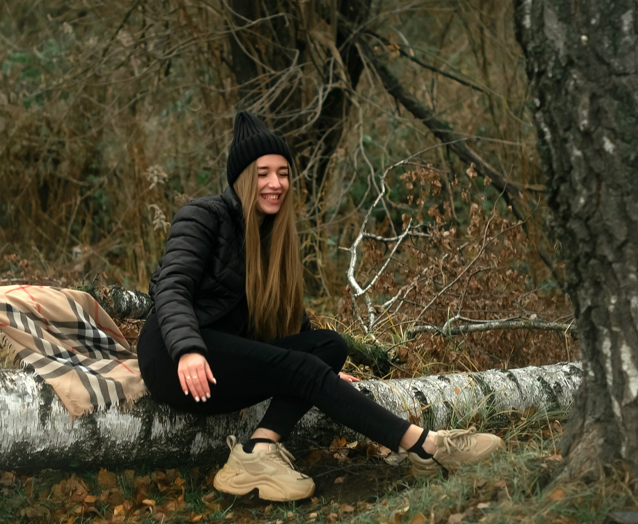 На фото девушка смеется в осеннем лесу.