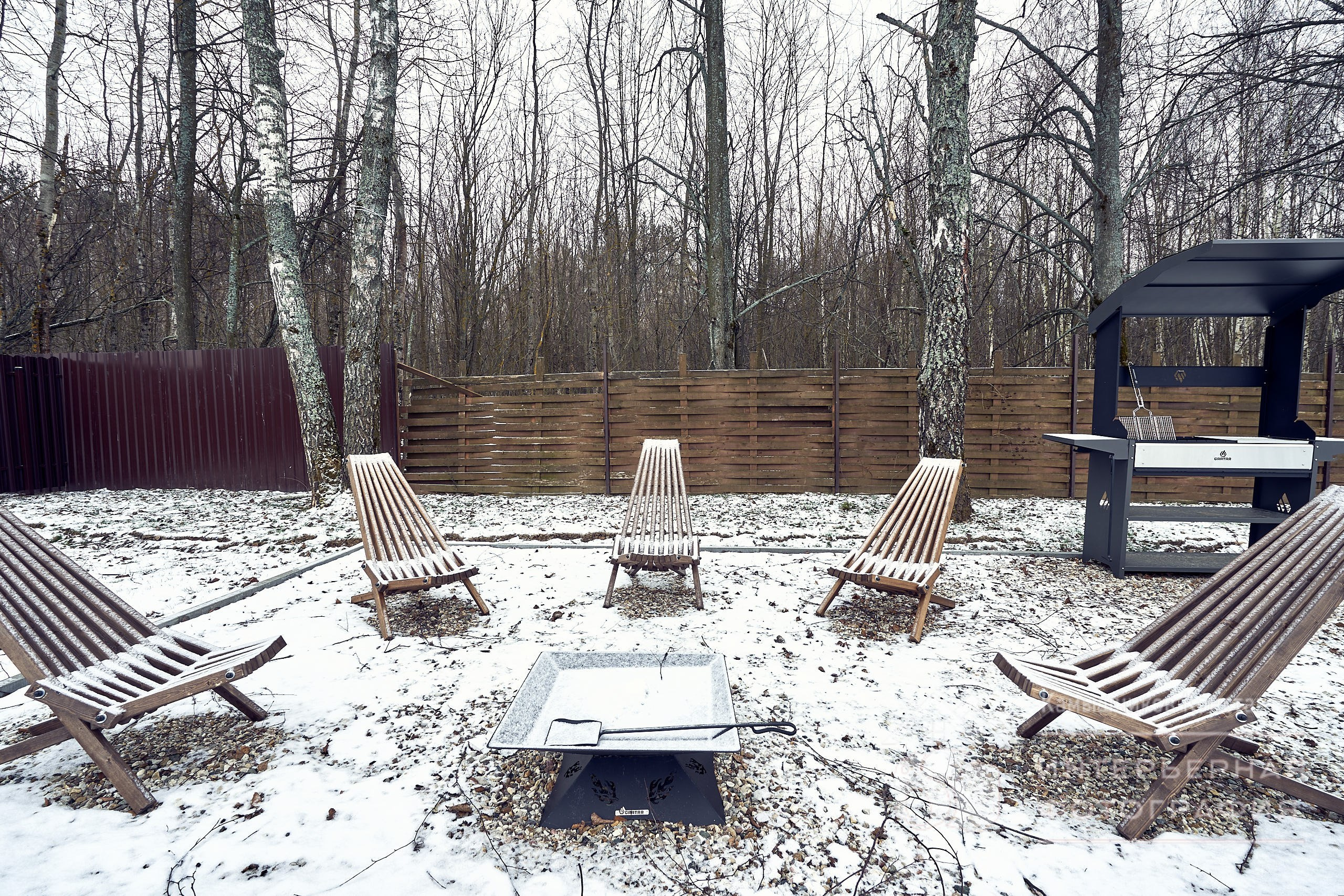 Архитектурная съемка садовых кресел у мангала на участке загородного дома в Подмосковье под покровом легкого первого снега