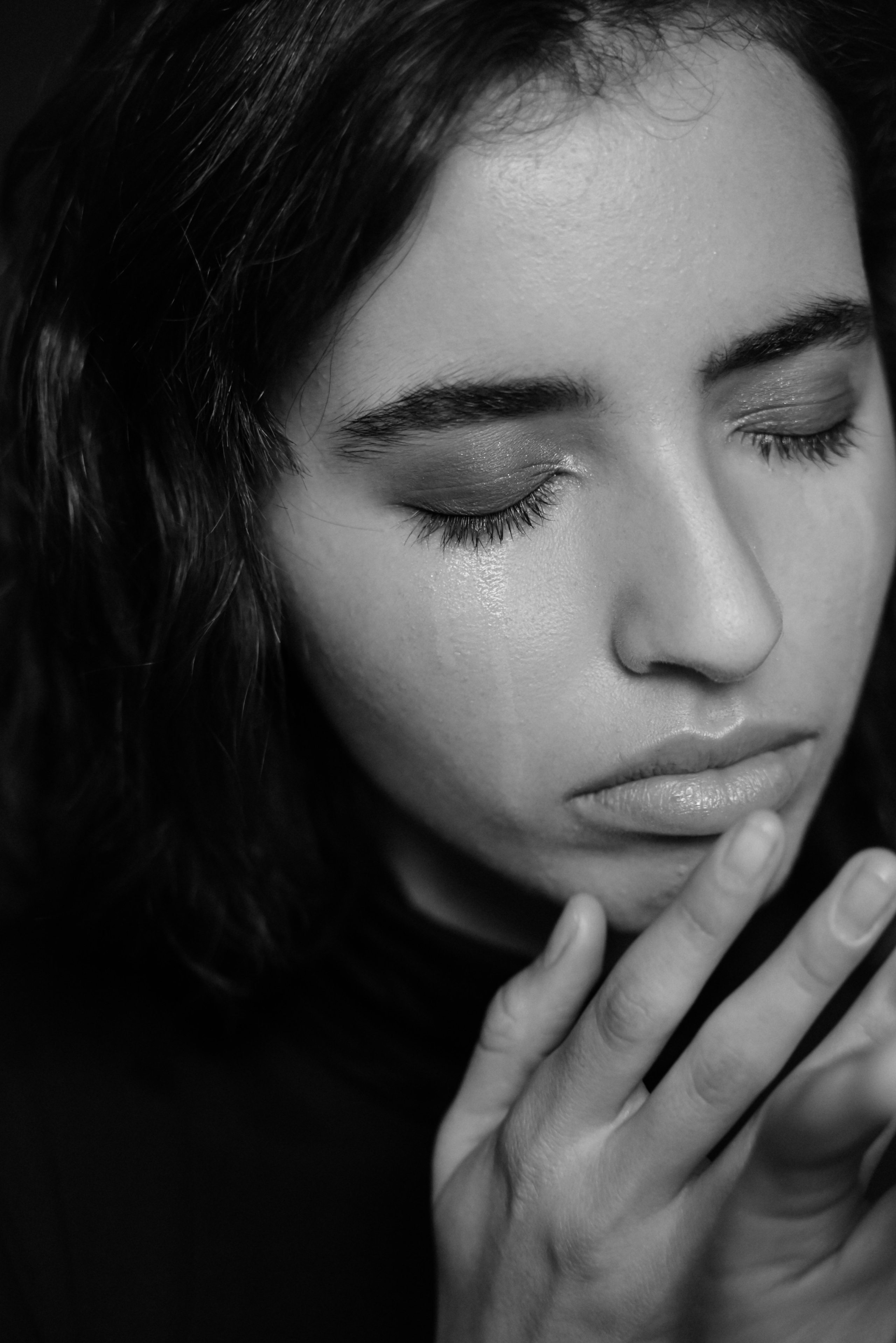 close-up portrait in black and white, woman with eyes closed and hand on chin, calm and meditative mood, tears