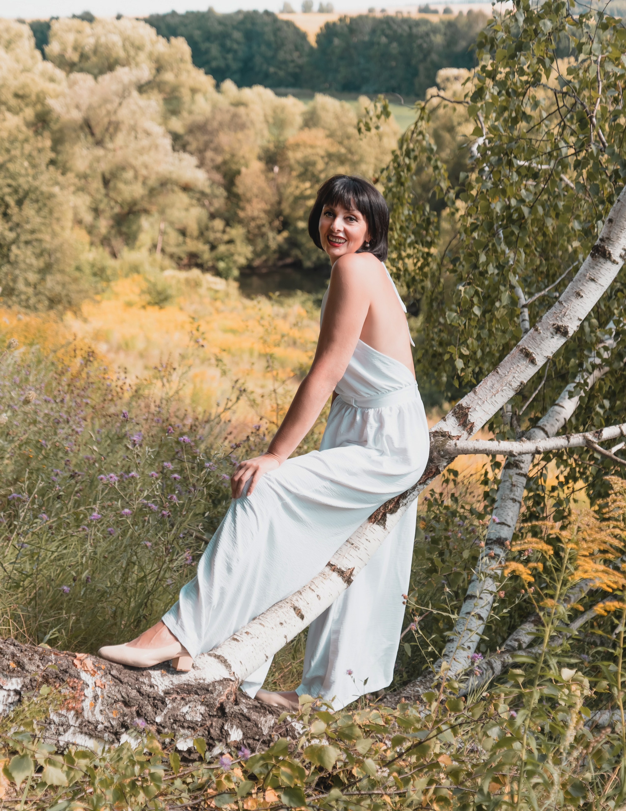 На фото девушка в лесу сидит на дереве.