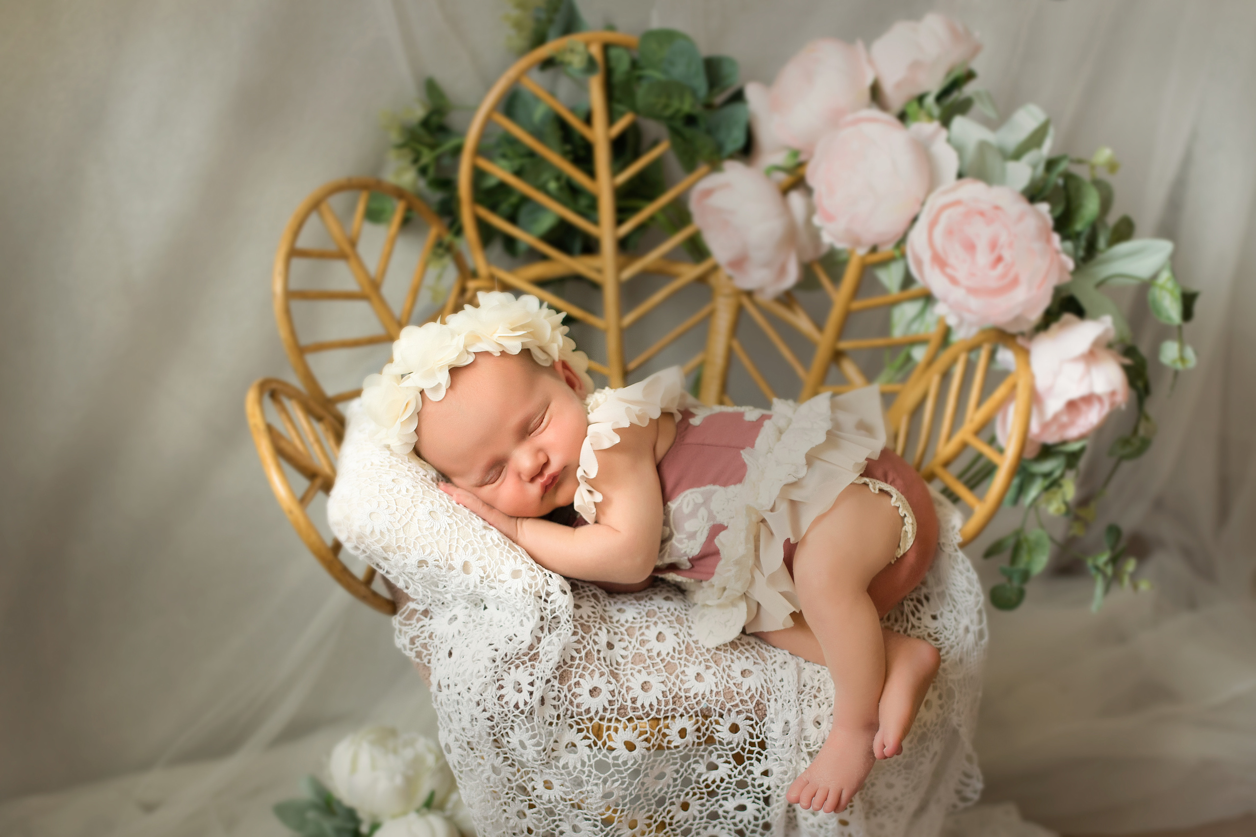 новорожденная девочка лежит на плетеном кресле с розами