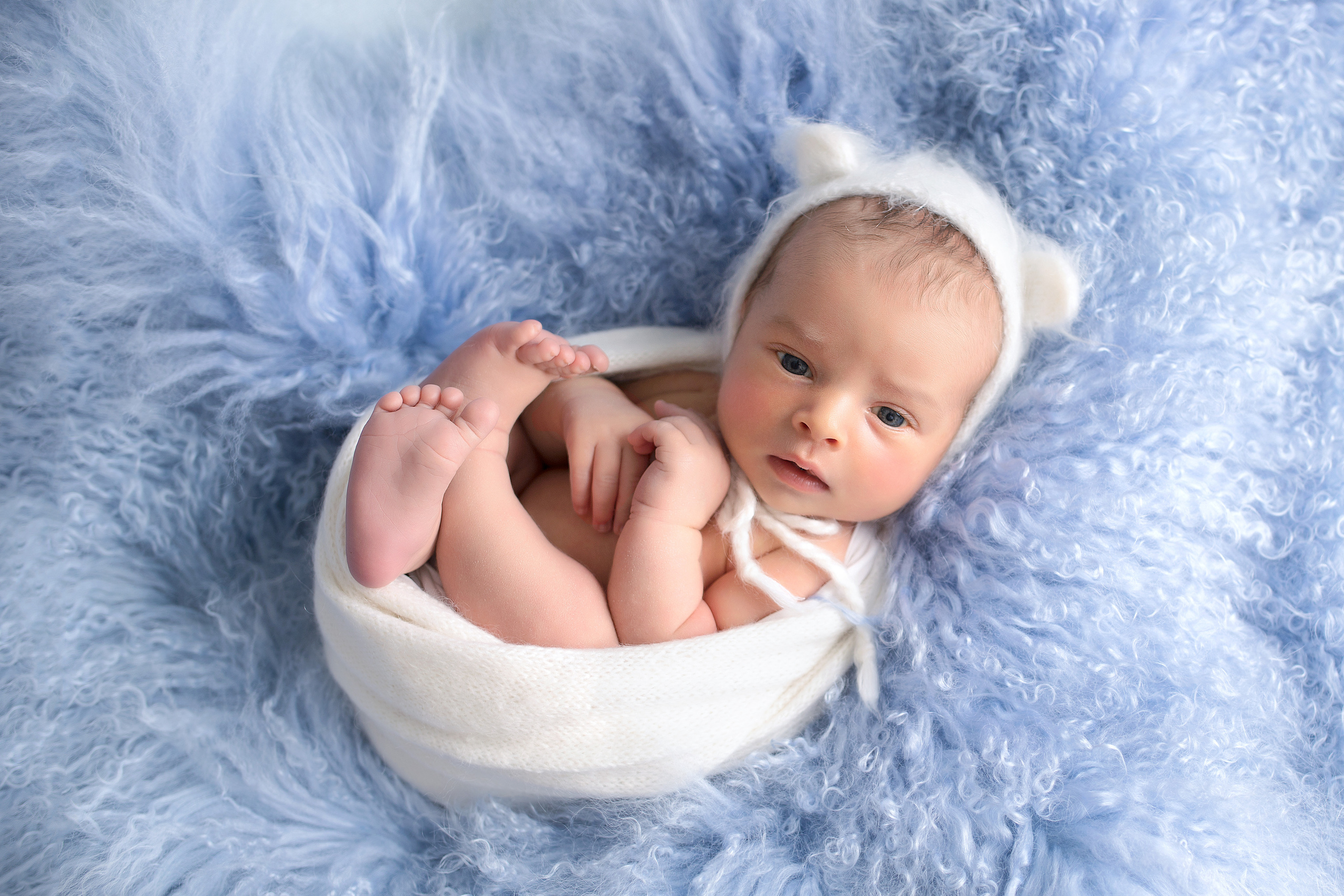 новорожденный мальчик в белой обмотке в шапочке с ушками на голубом меховом пледе