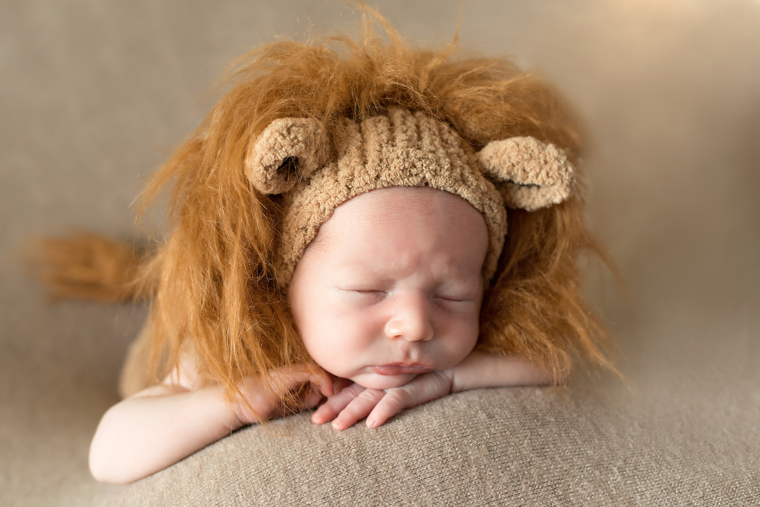 новорожденный в костюме львенка с ручками под подбородок