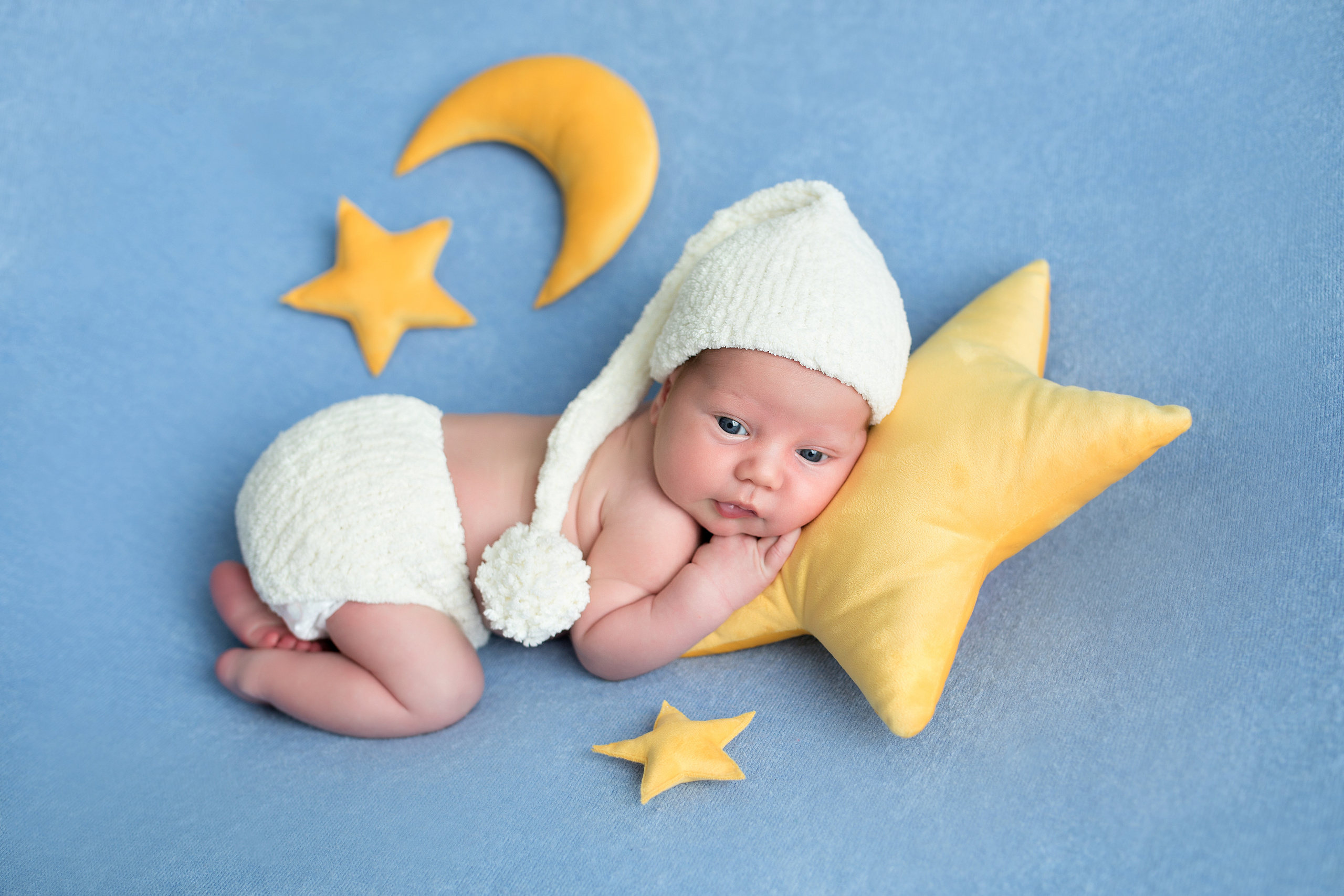 новорожденный в костюме гномика в белом колпачке на подушке в форме звезды на голубом фоне