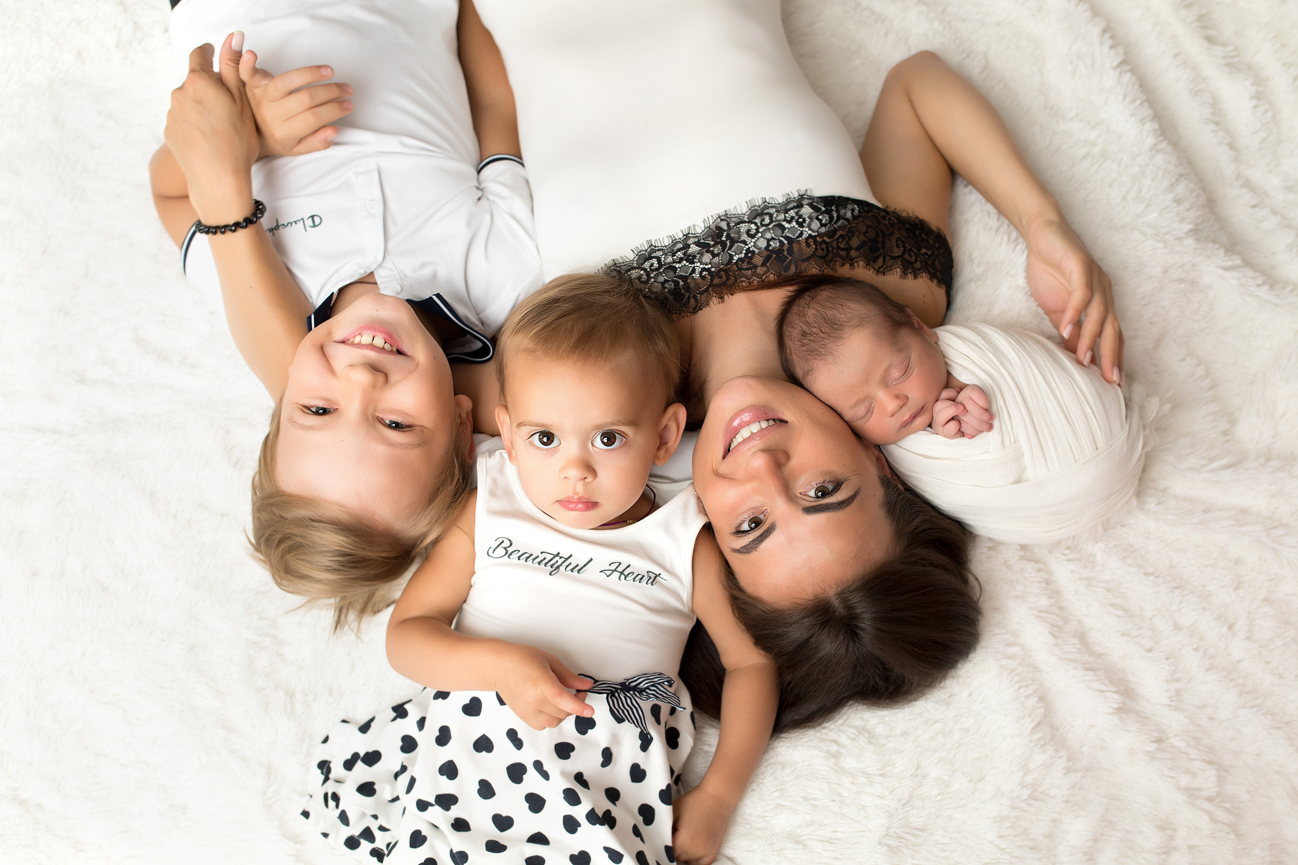 мама с тремя детьми лежат на ковре с новорожденным малышом