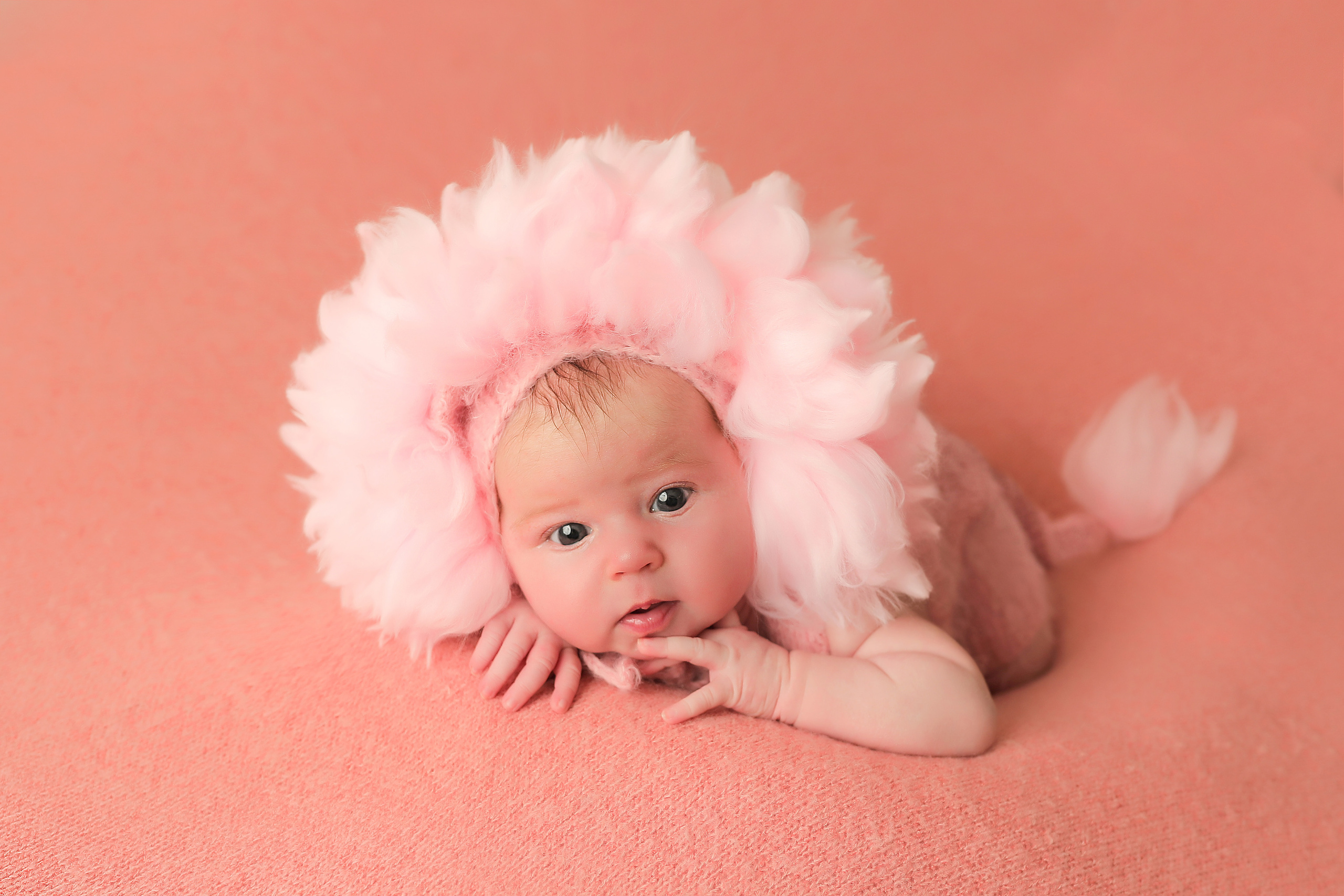 новорожденная девочка в костюме розового львенка на розовом фоне